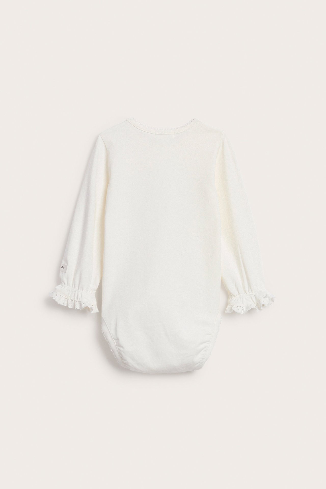 Rückenansicht eines cremeweißen, einfarbigen Baby-Bodys aus Jersey mit Picot-Ausschnitt und Spitzenrüschen an den Ärmelbündchen.