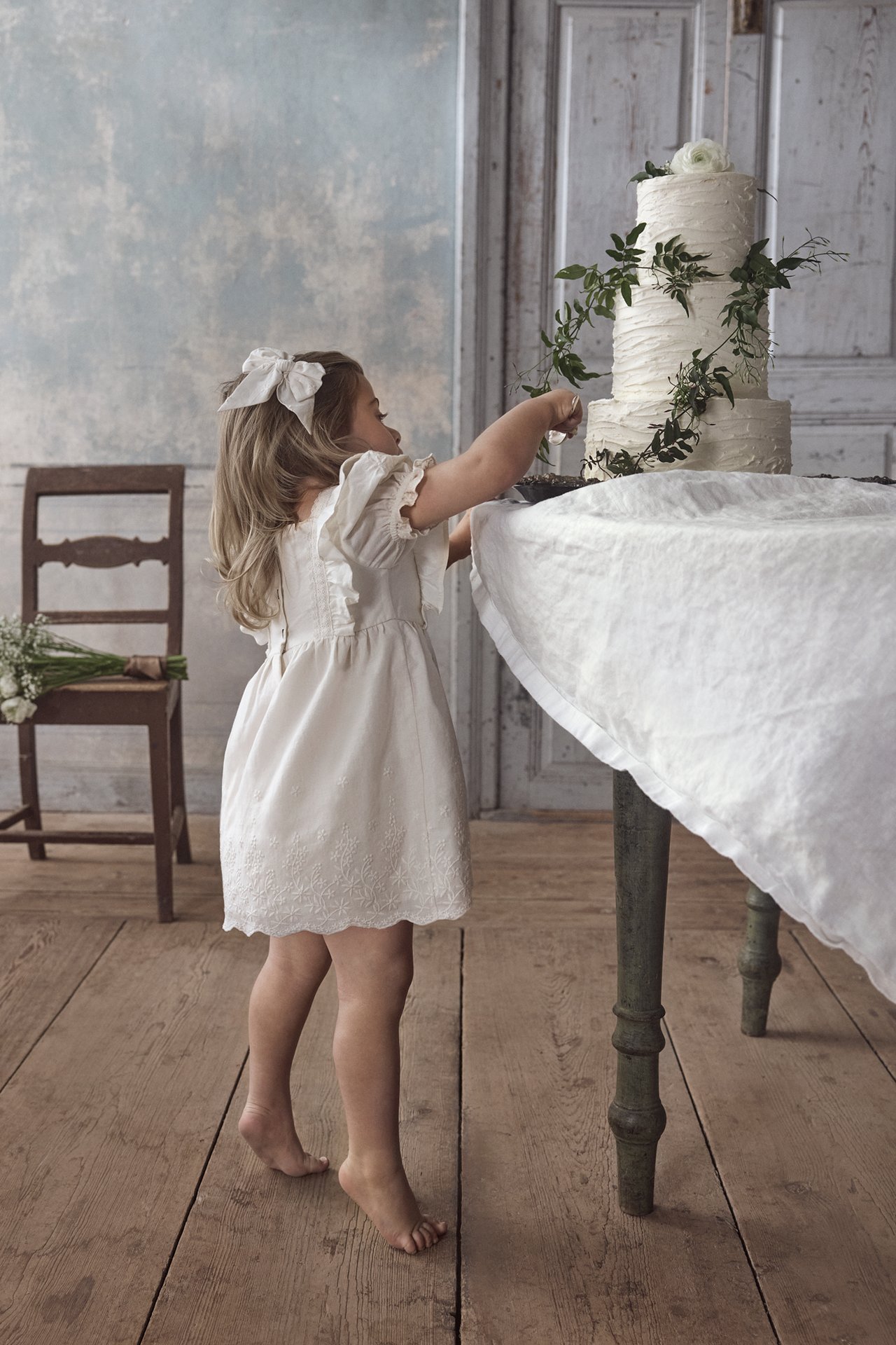 Side view of a kid in an offwhite embroidered cotton dress with frills, puff sleeves, and a white hair bow.