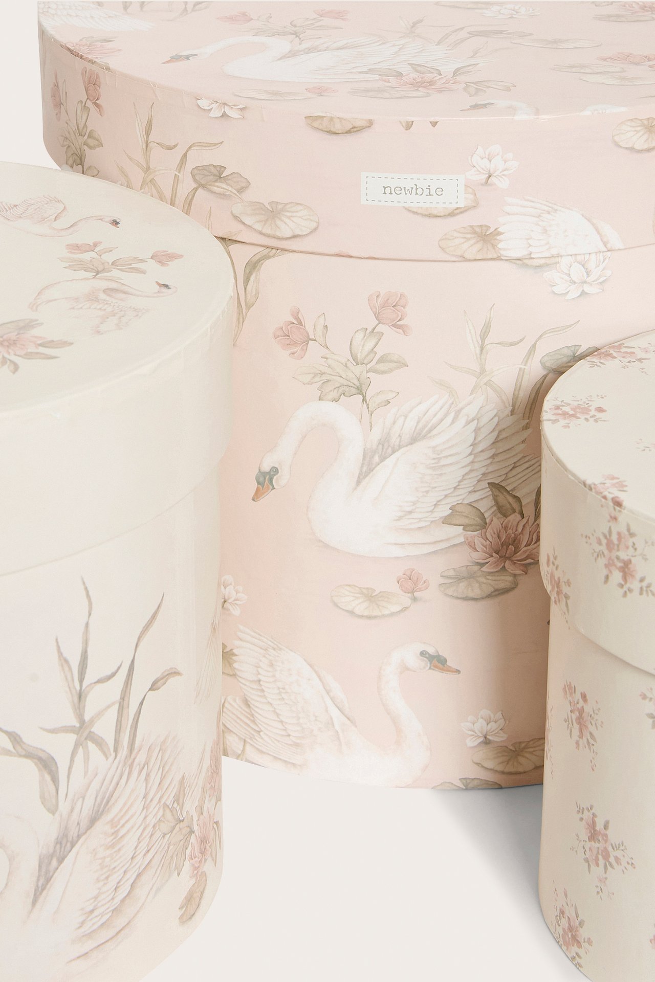 Front view of three round paper storage boxes with lids, featuring white swans and pink floral patterns.