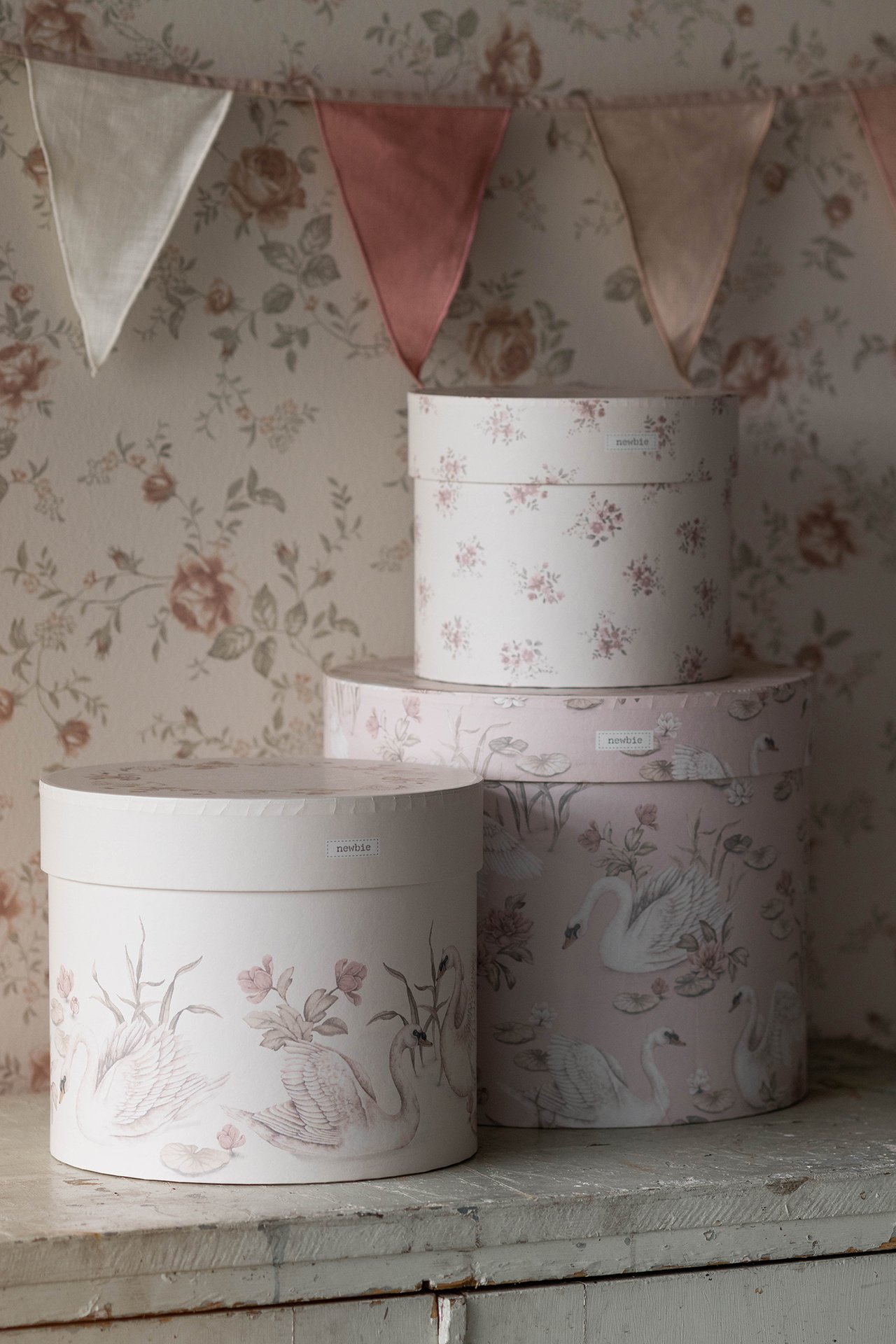 Front view of three stacked round white and pink paper storage boxes with lids, featuring floral and swan patterns.
