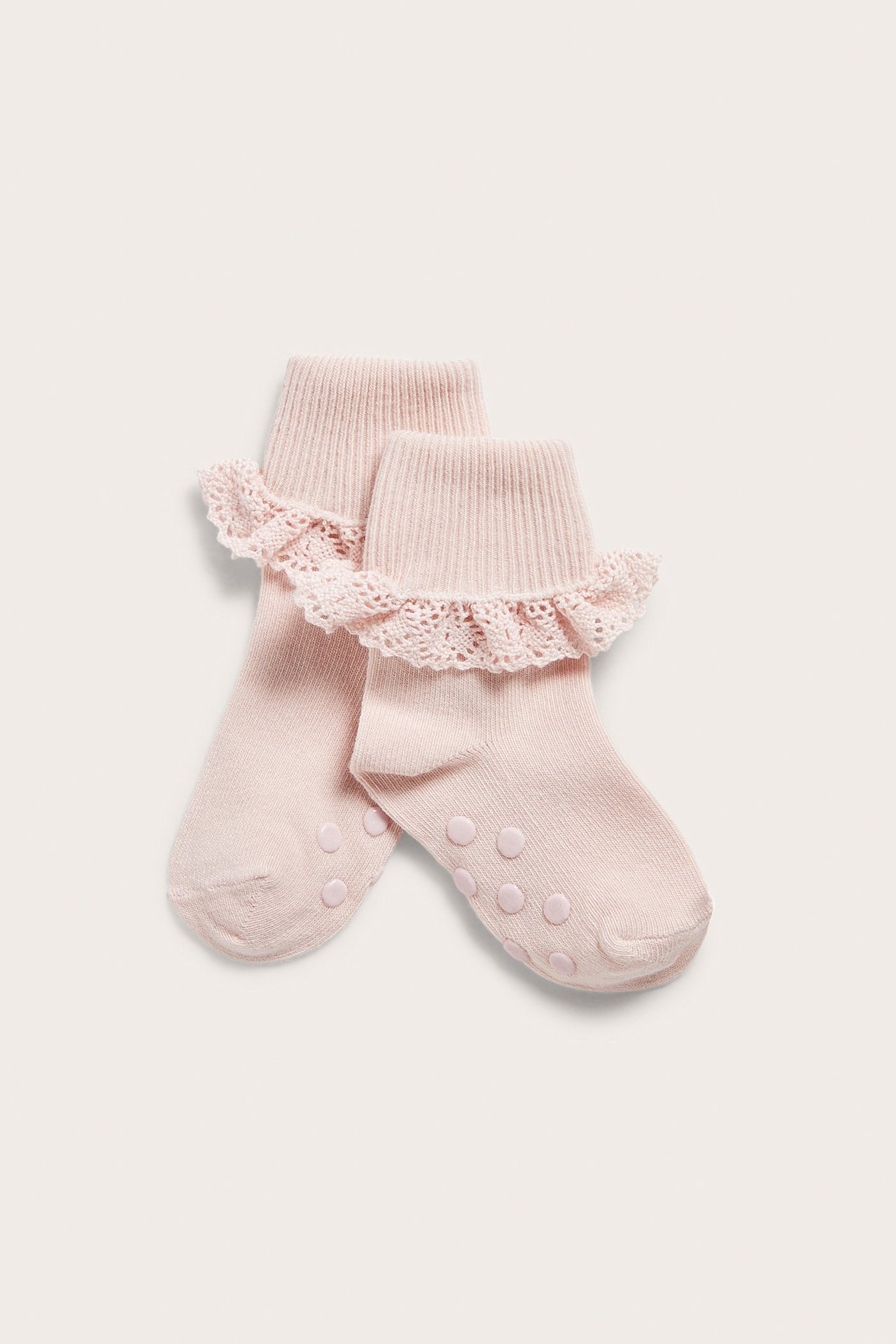 Close-up of two light pink baby socks with ribbed cuffs, lace ruffles, and anti-slip dots on soles.