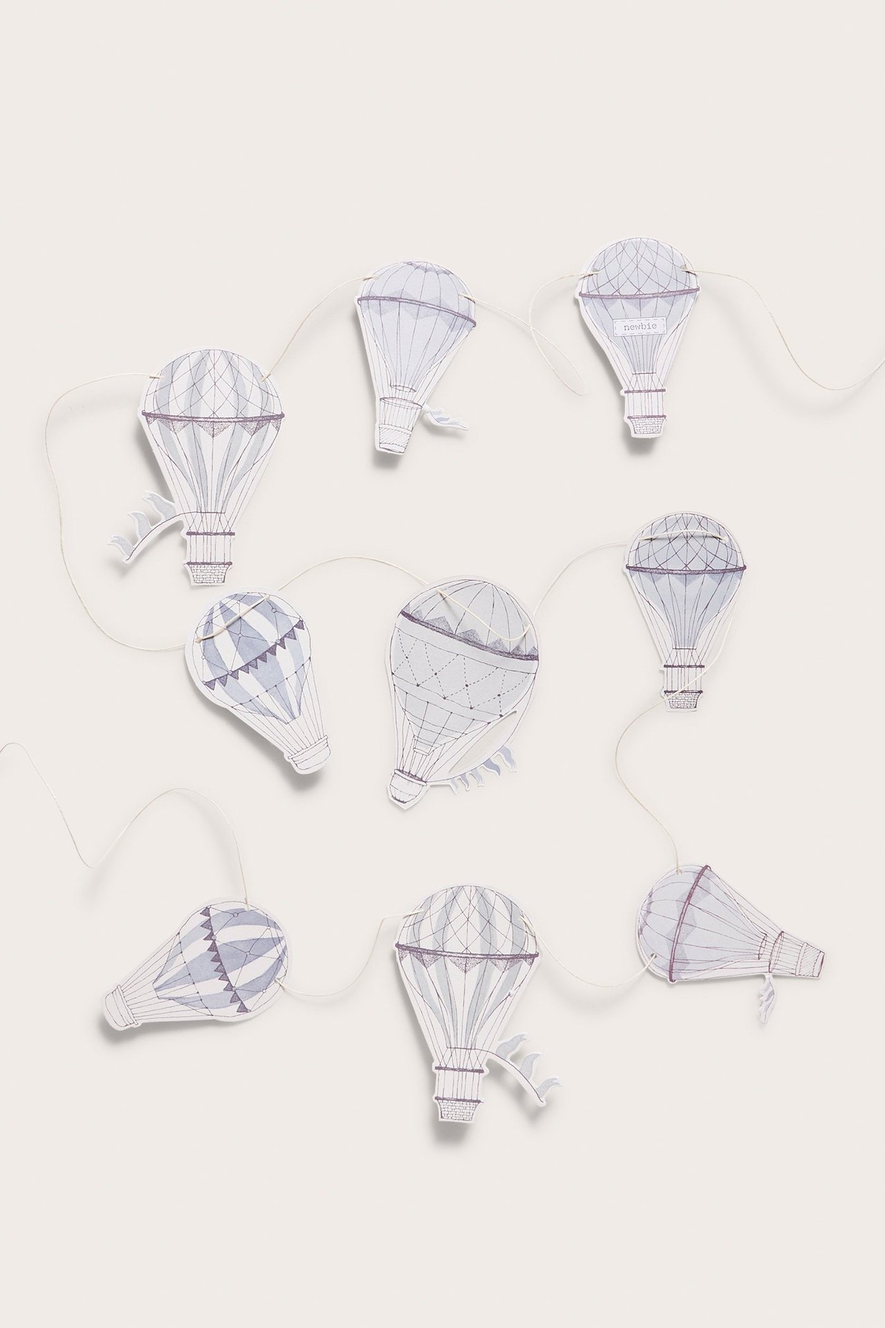 Draufsicht auf eine cremefarbene Papiergirlande mit neun gemusterten hellblauen Heißluftballons an einer Schnur.