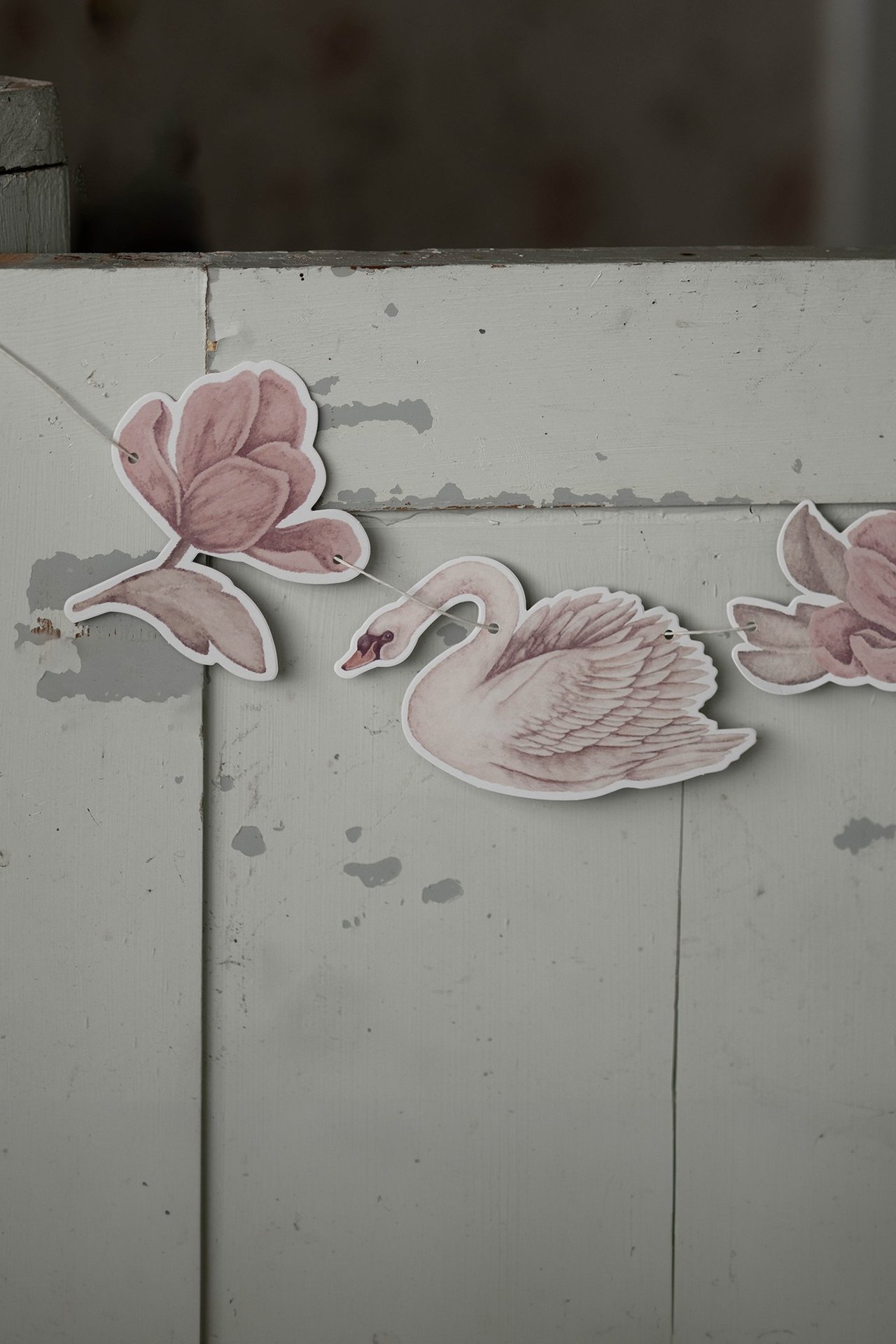 Nahaufnahme einer cremefarbenen Papiergirlande mit Schwan- und rosa Blumenmotiven an einer Schnur.