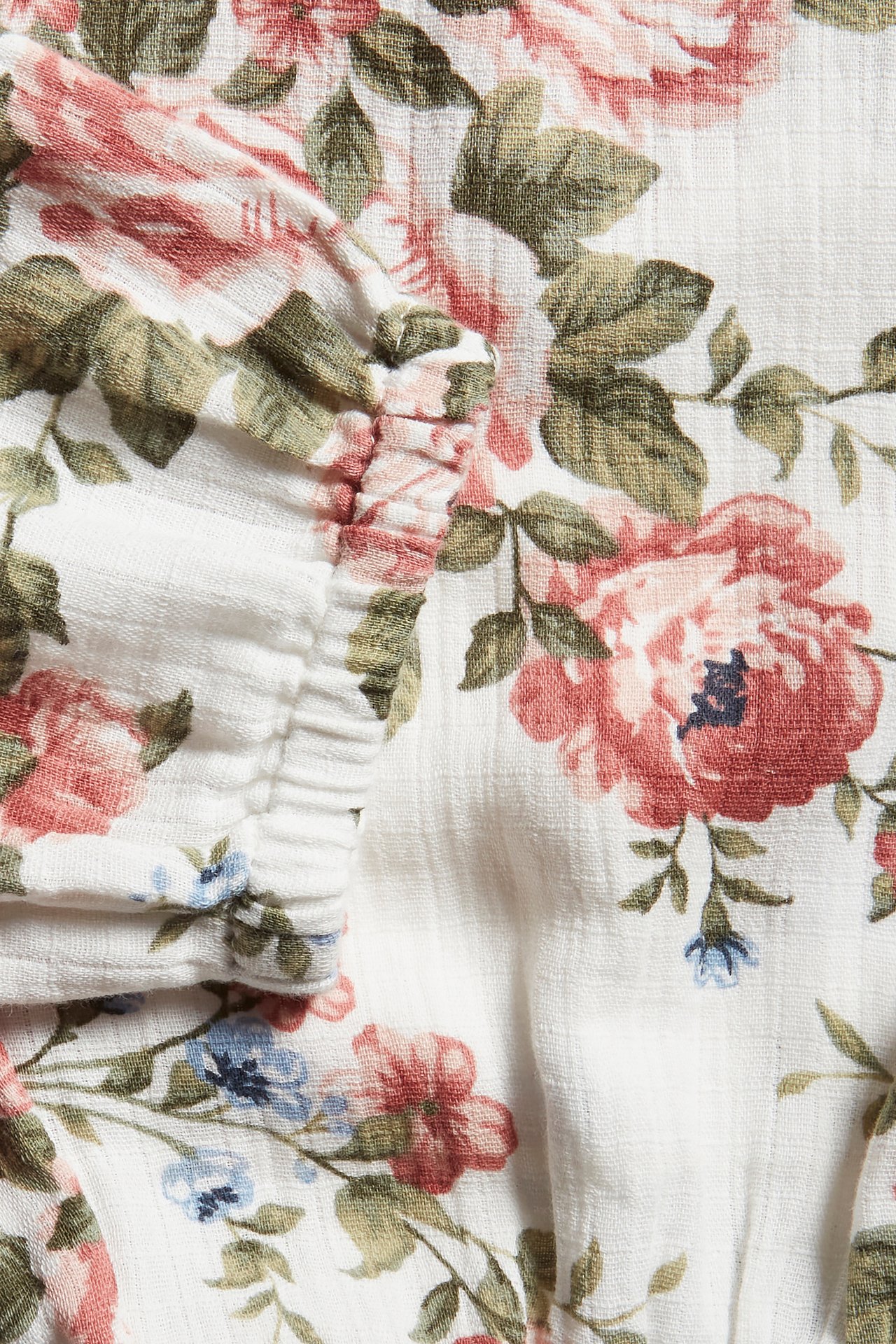 Close-up of off-white baby pants with pink rose and green leaf floral pattern, showing elasticated detail.
