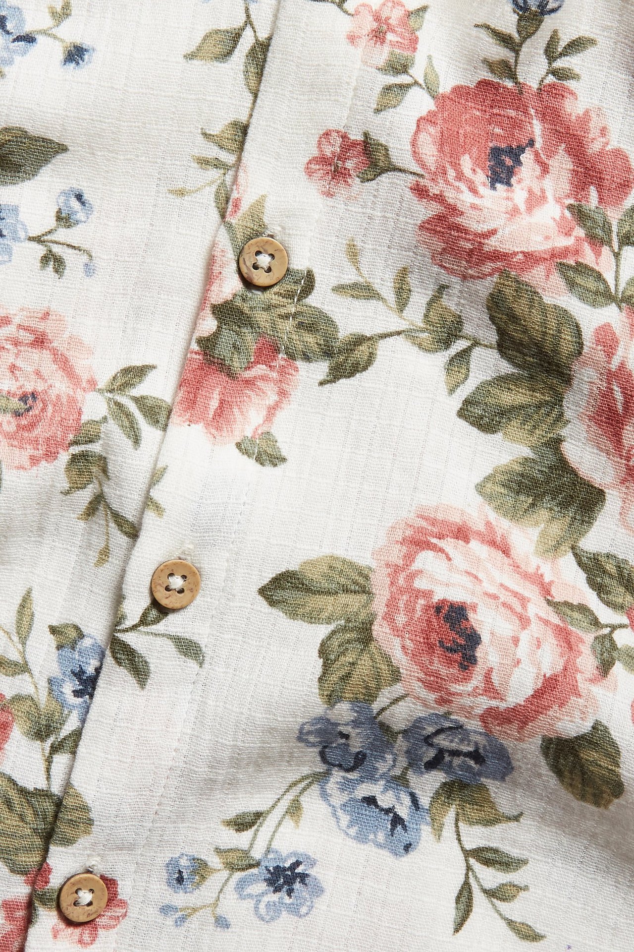 Close-up of an off-white woven cotton fabric with a pink and blue floral pattern and wooden buttons.