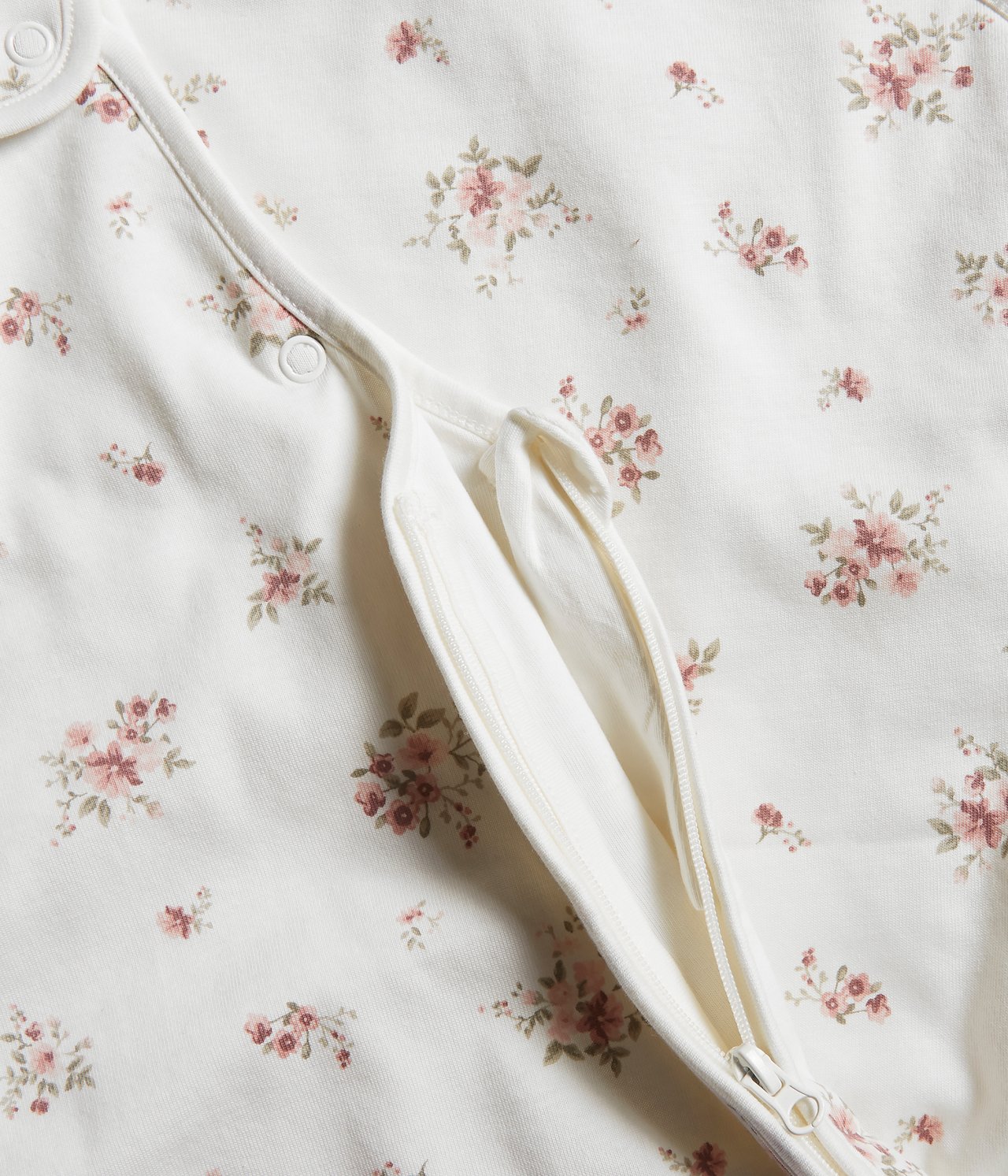 Close-up of a pink floral patterned baby sleeping bag with a partially unzipped two-way zipper and snap buttons.