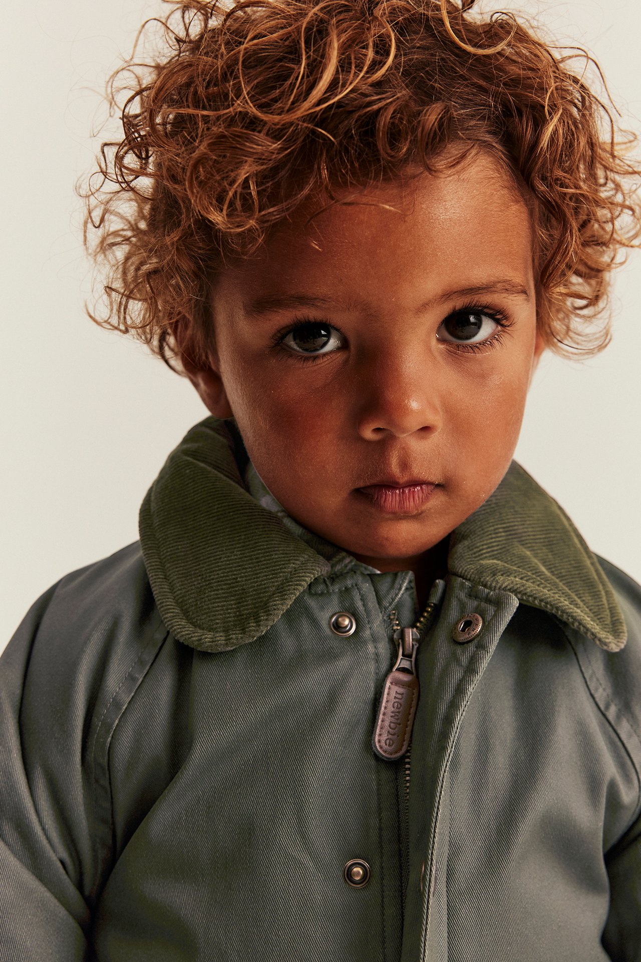 Close-up of a kid wearing an olive green jacket with a corduroy collar, zipper, and snap buttons.