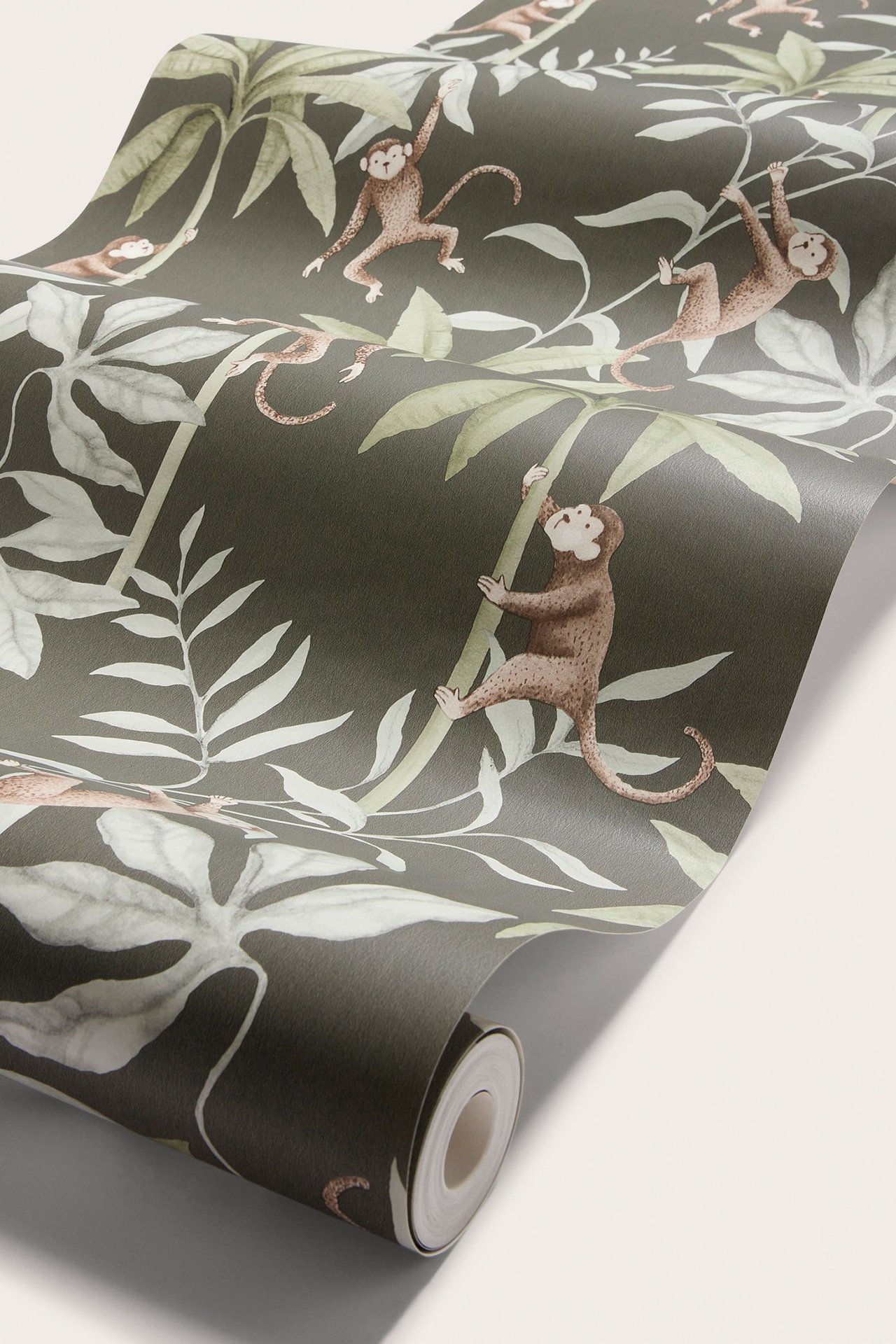 Nahaufnahme einer Tapetenrolle mit dunkelgrünem Blatt- und braunem Affenmuster.