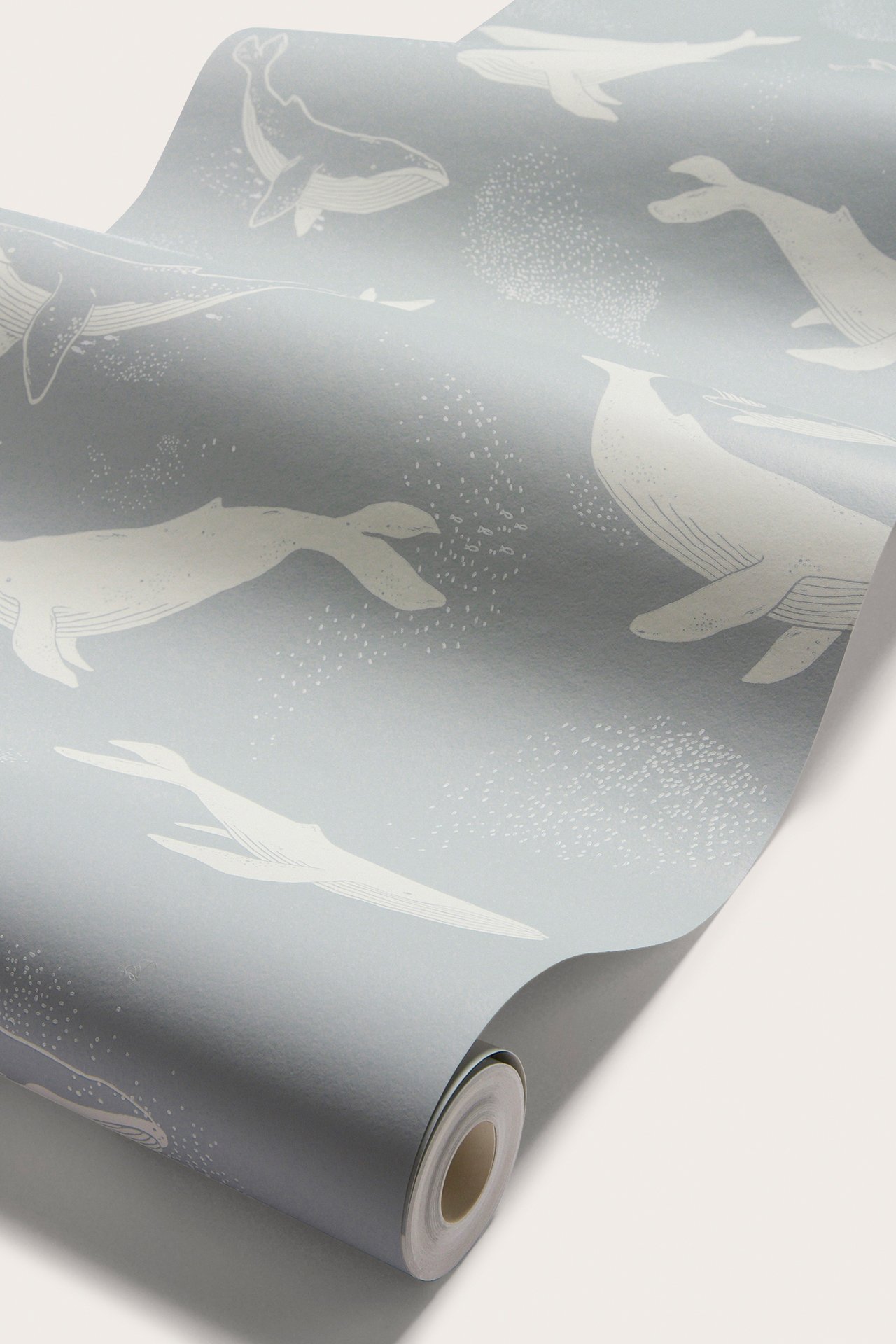 Nahaufnahme einer hellblauen Tapetenrolle mit Muster aus weißen Walen und kleinen Punkten.
