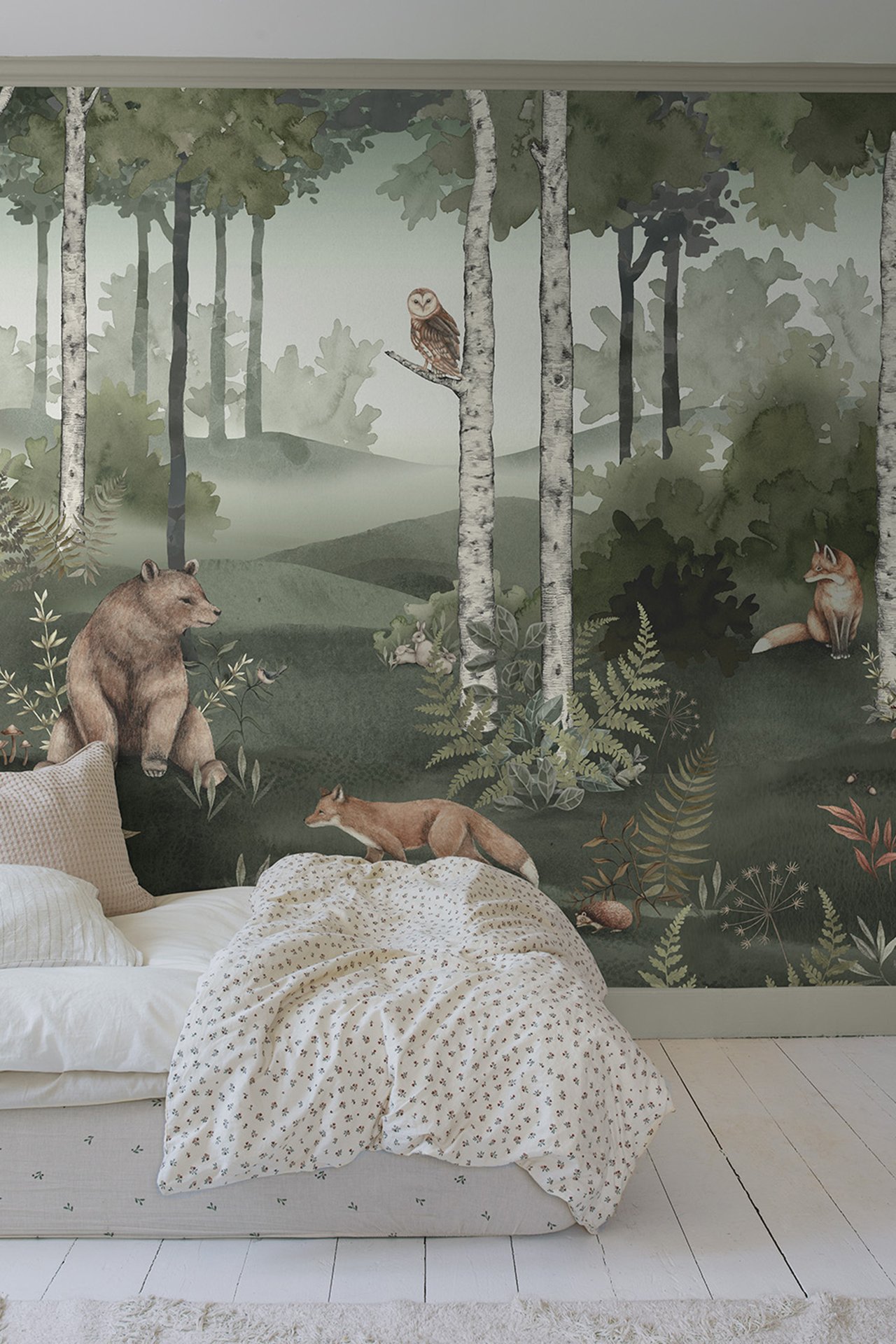 Green forest animal patterned wallpaper mural with trees, foxes, bears, and an owl above a bed.