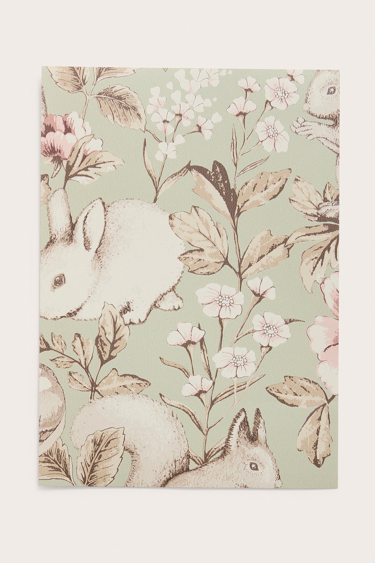 Nahaufnahme einer grünen Tapetenprobe mit weißen Kaninchen, Eichhörnchen, rosa-weißen Blumen und braunen Blättern.