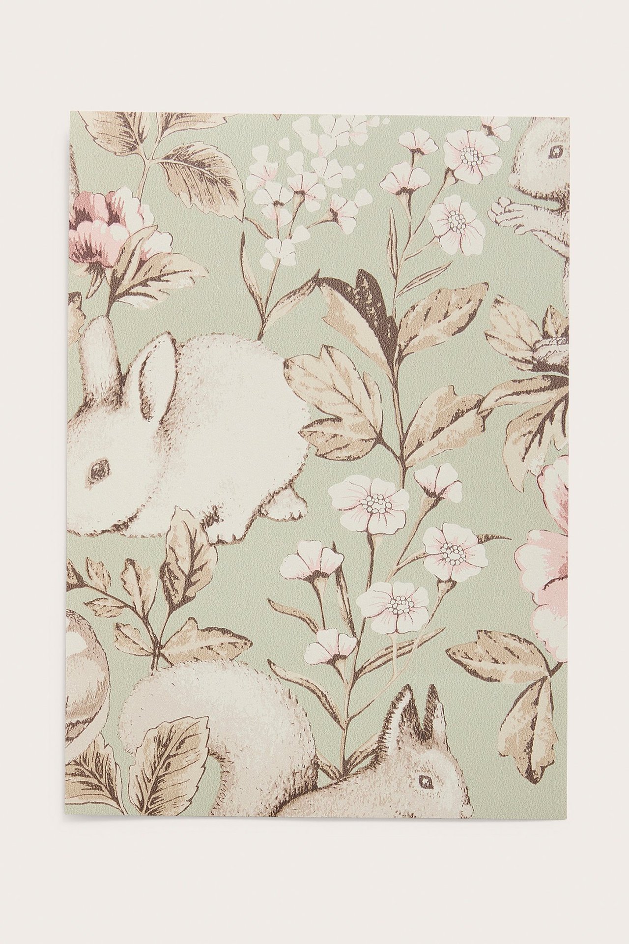 Nahaufnahme einer grünen Tapetenprobe mit weißen Kaninchen, Eichhörnchen, rosa-weißen Blumen und braunen Blättern.