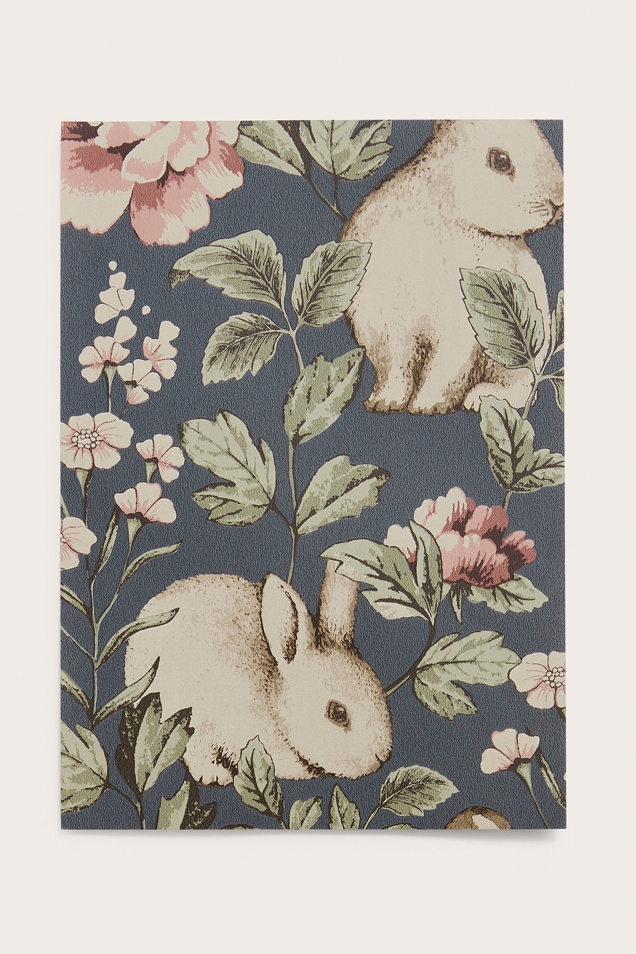 Nahaufnahme einer blauen Mustertapete mit weißen Kaninchen, grünen Blättern und rosa Blumen.