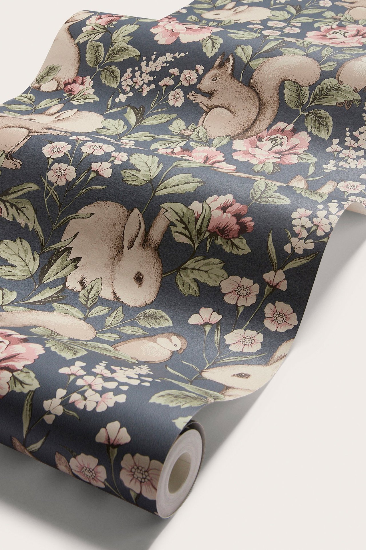 Nahaufnahme einer blauen Vliestapete mit Muster aus beigen Hasen, Eichhörnchen, Vögeln und rosa Blumen.