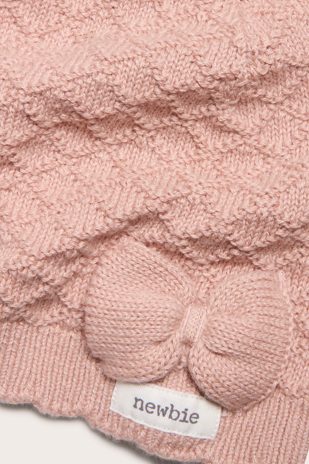 Nahaufnahme einer rosa gemusterten Baumwollstrickmütze für Baby/Kind, mit Schleife und Rippbündchen.