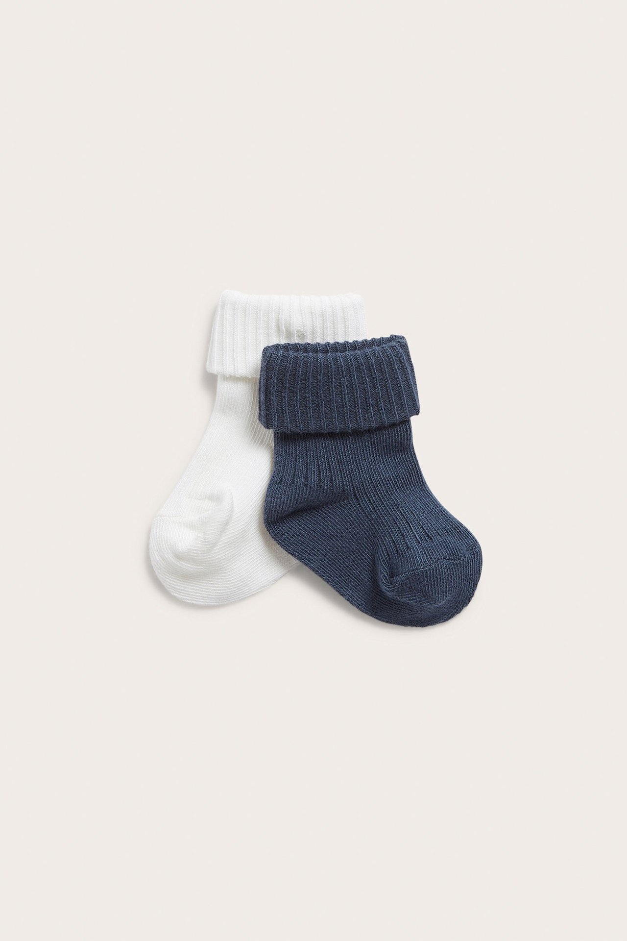 Vorderansicht von zwei gerippten Babysocken, eine dunkelblau und eine weiß, mit umgeschlagenen Bündchen.