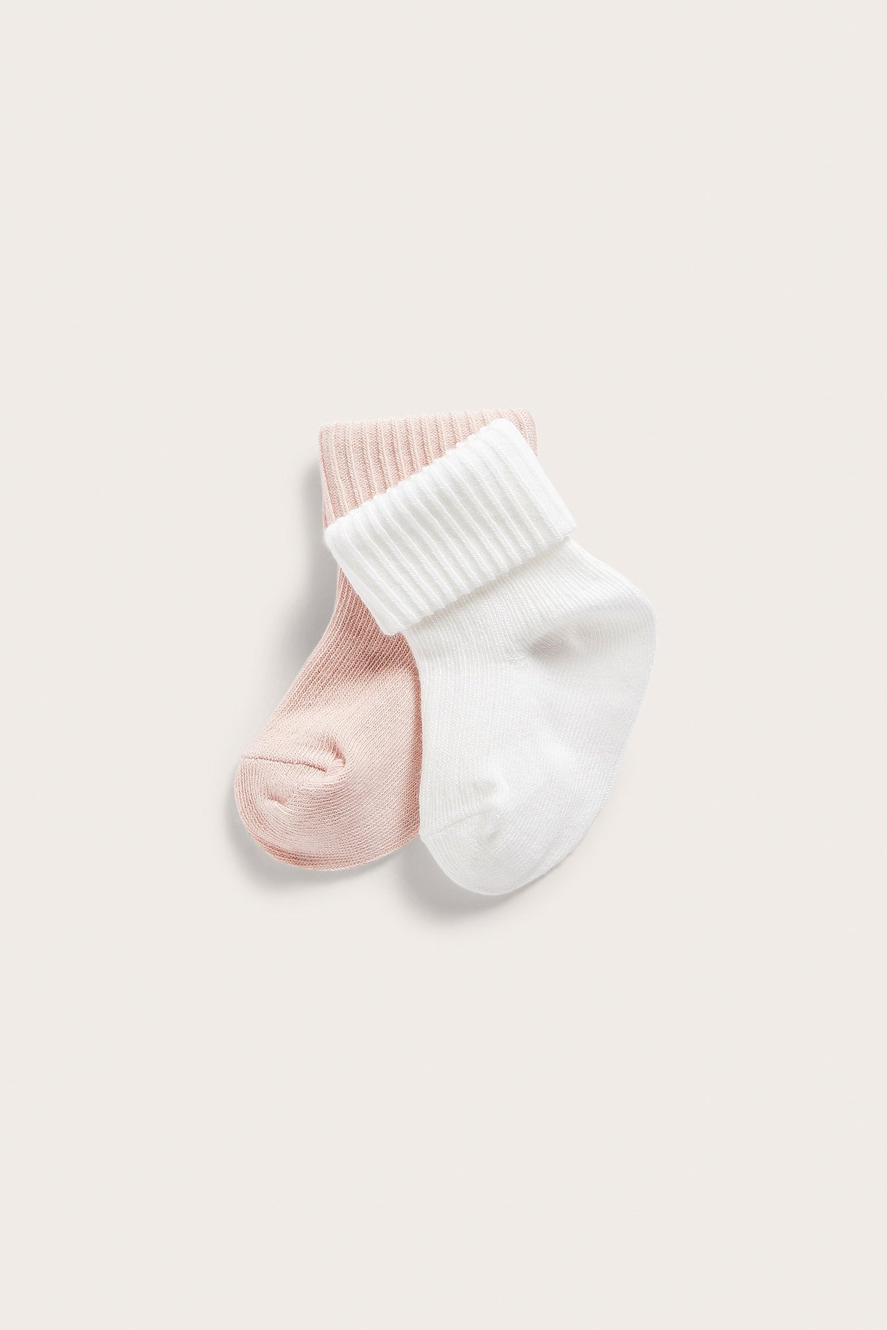 Close-up of two solid baby socks: one light pink and one white, both with ribbed cuffs.