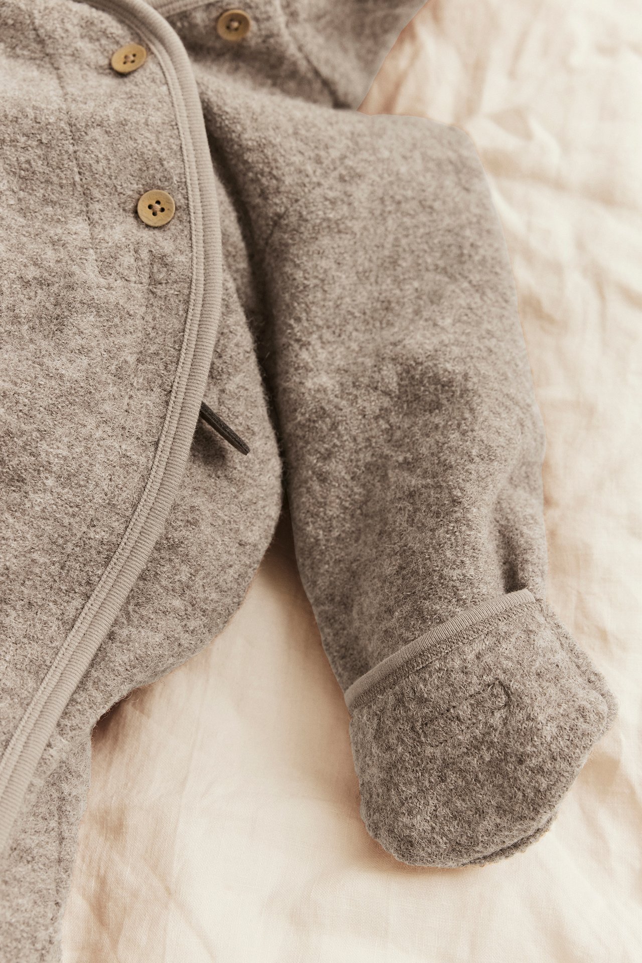 Close-up of a gray felt baby coat with wooden buttons and ribbed binding.