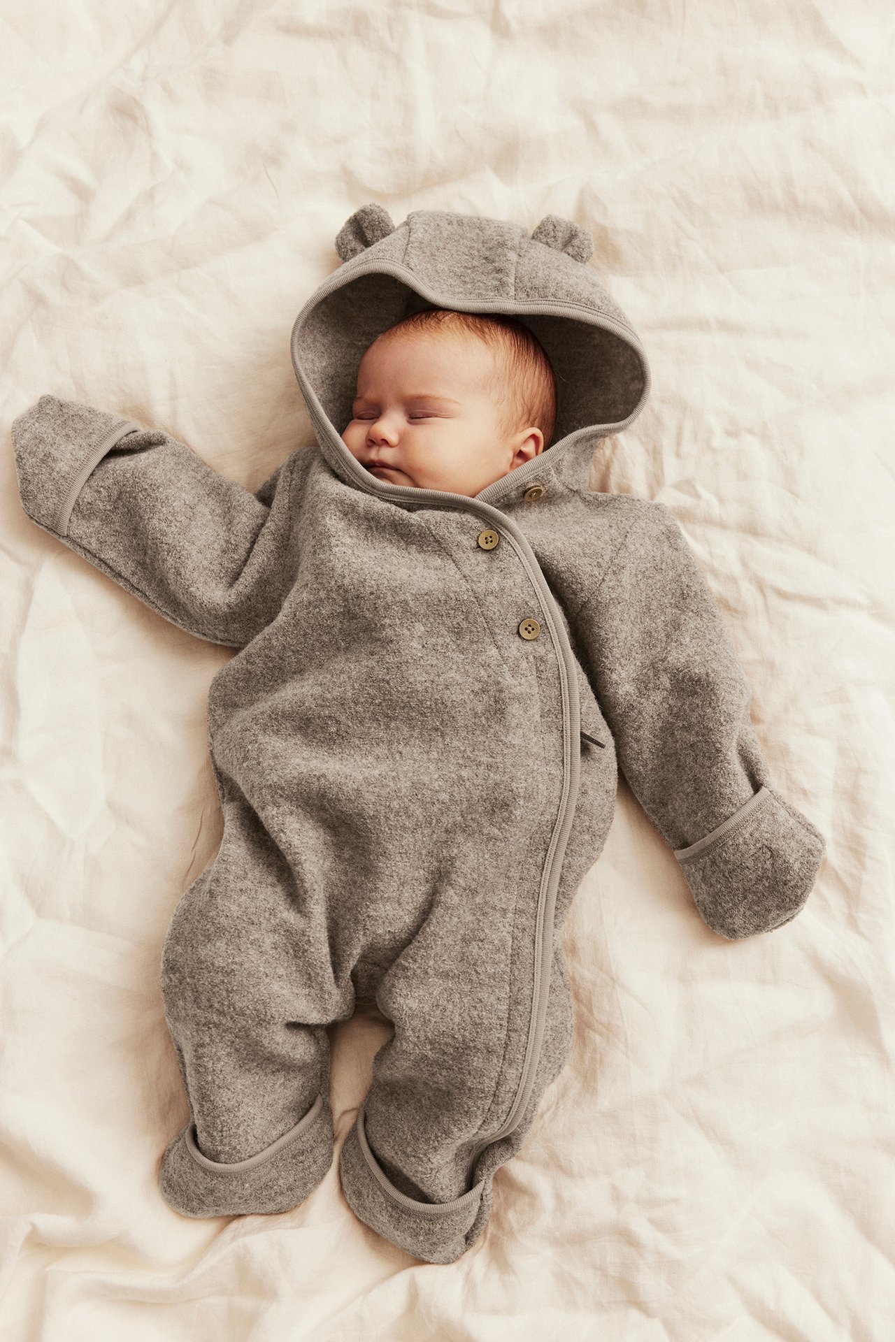 Sleeping baby wears a gray hooded fleece romper with bear ears, buttons, and a zipper.