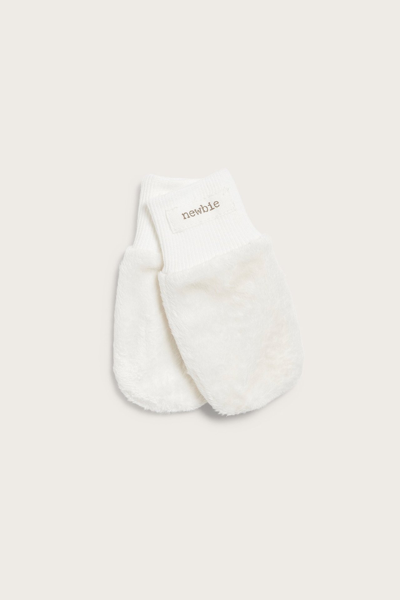 Front view of offwhite baby mittens with soft faux fur and ribbed cuffs, featuring a 'newbie' label.