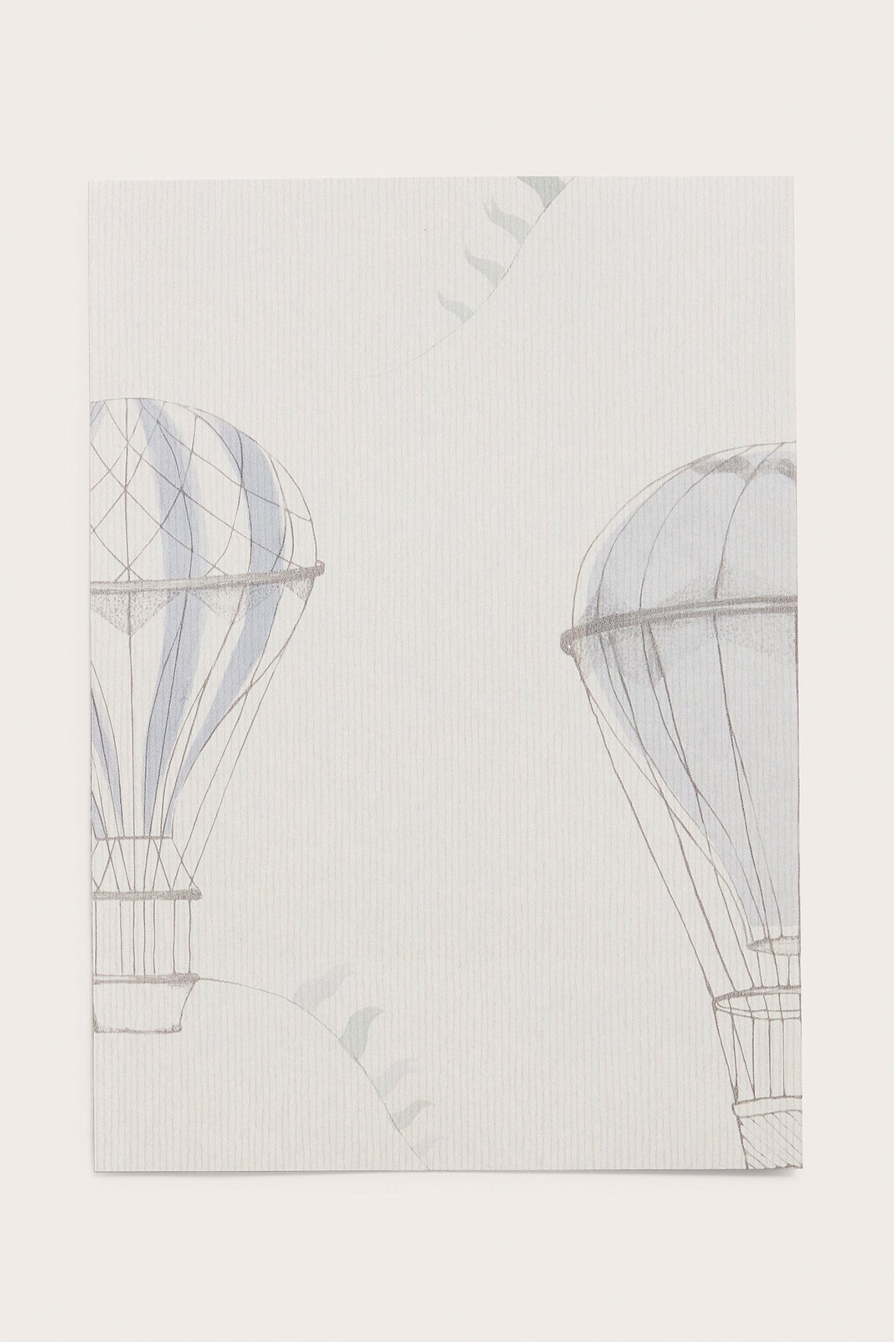 Close-up of a grey wallpaper sample with light blue hot air balloon and flag patterns.