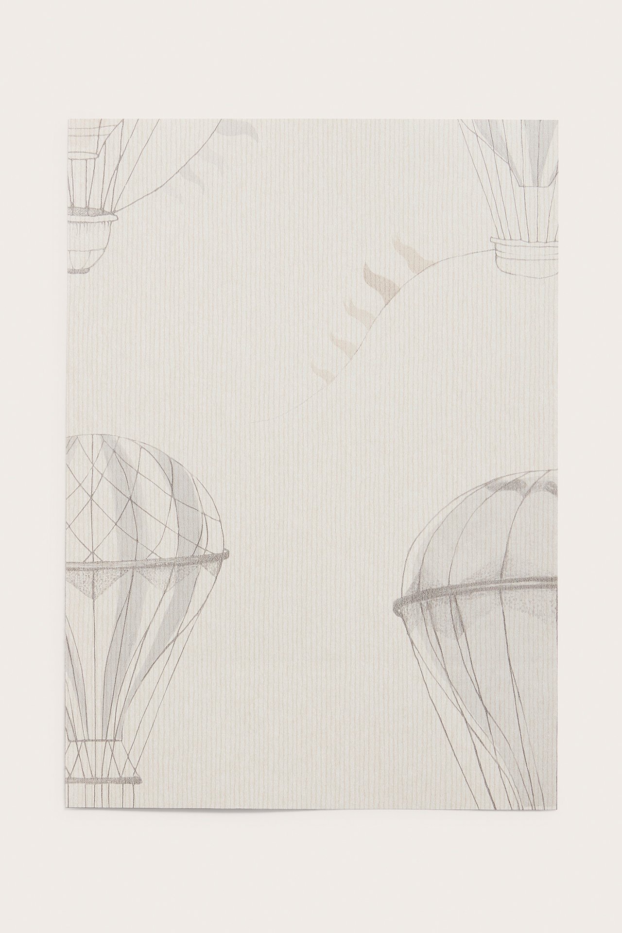 Close-up of a beige non-woven wallpaper sample with a light grey hot air balloon pattern.