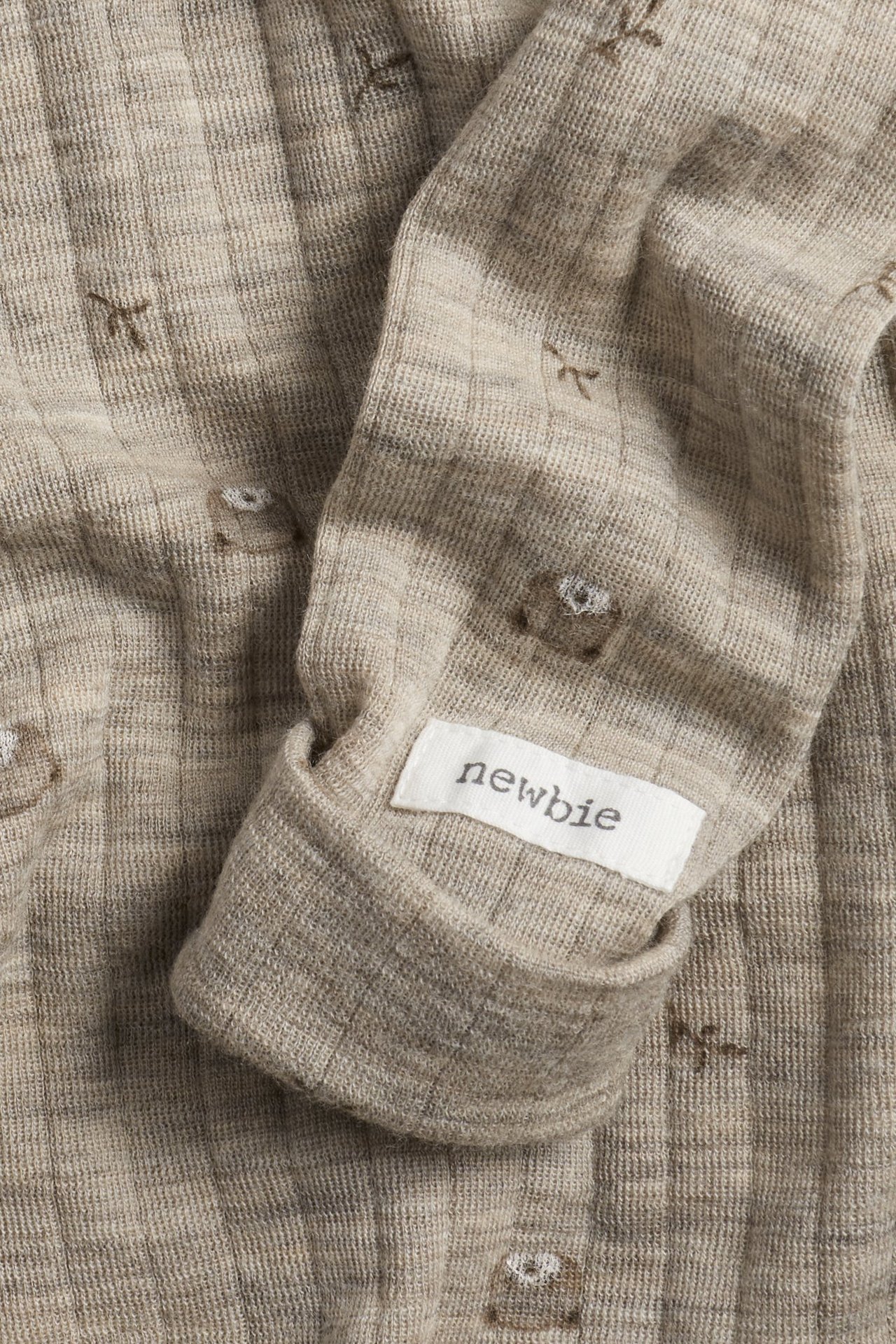 Close-up of a beige melange ribbed wool baby bodysuit with a teddy bear pattern and folded cuff.