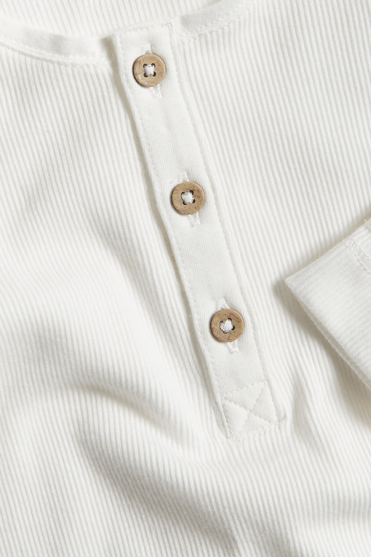 Close-up of a white ribbed long-sleeve Henley top with three wooden buttons.