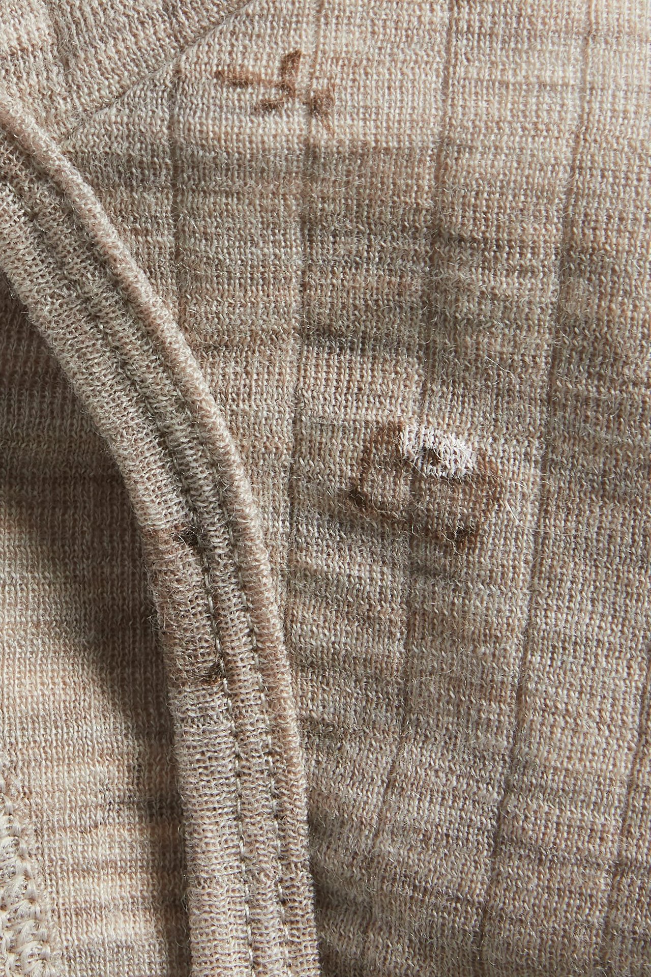 Close-up of beige melange wool baby bonnet fabric with faint teddy bear print.