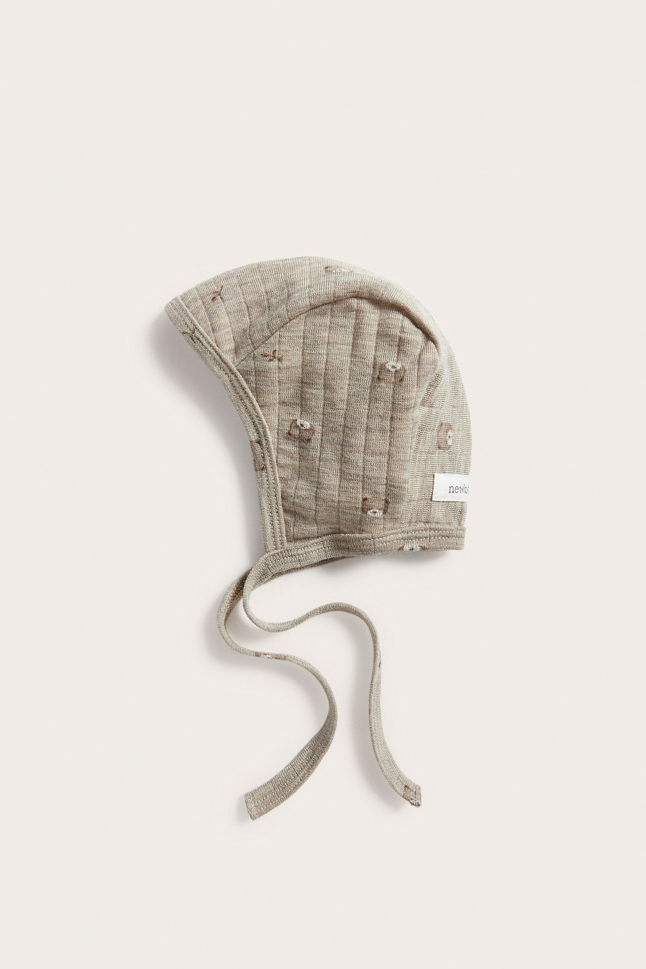 Flachgelegte hellbeige gerippte und gesteppte Babyhaube mit gestickten Tieren und Bindebändern.