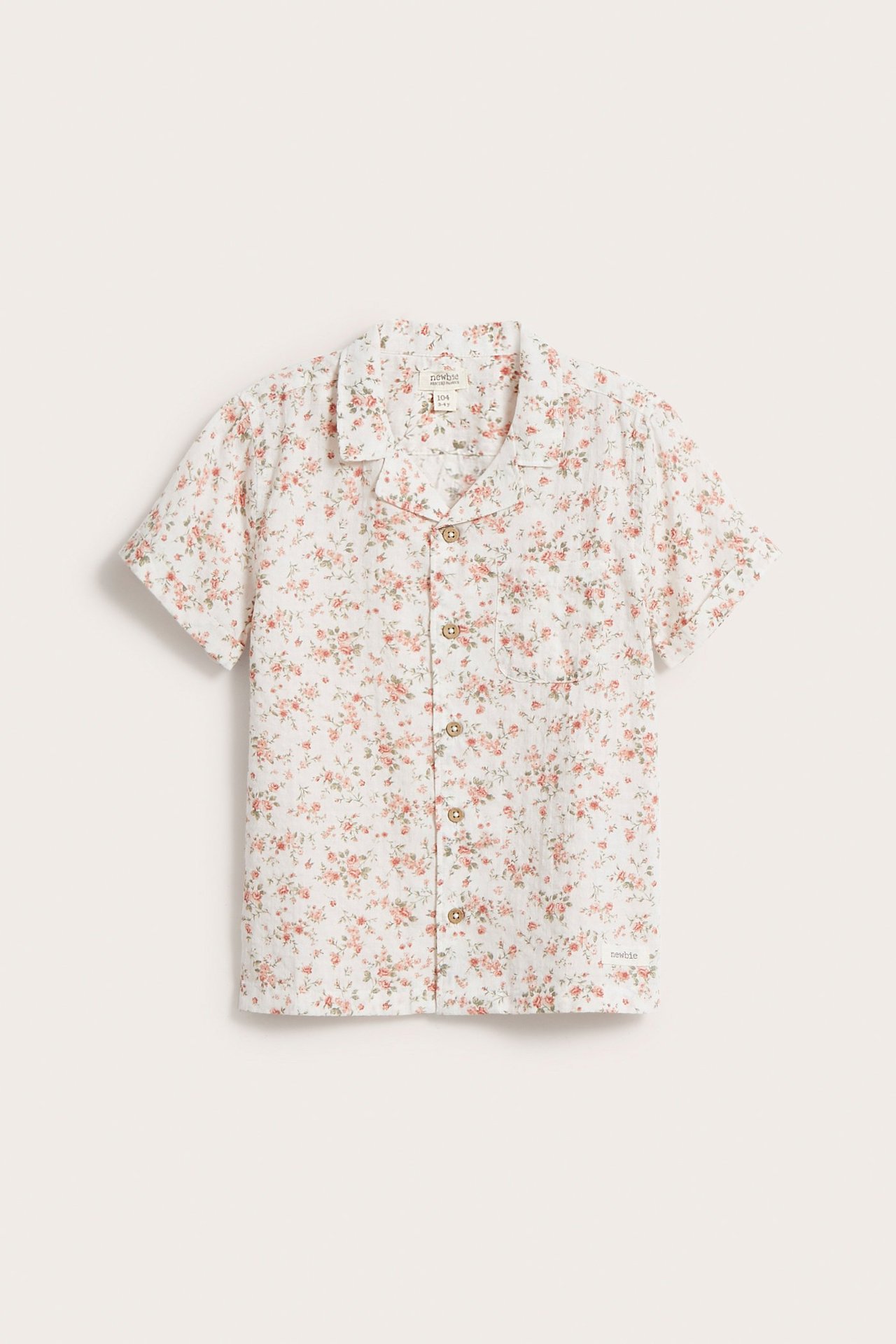 Front view: Kid's white cotton short-sleeve shirt with pink floral pattern, lapel collar, pocket, and buttons.