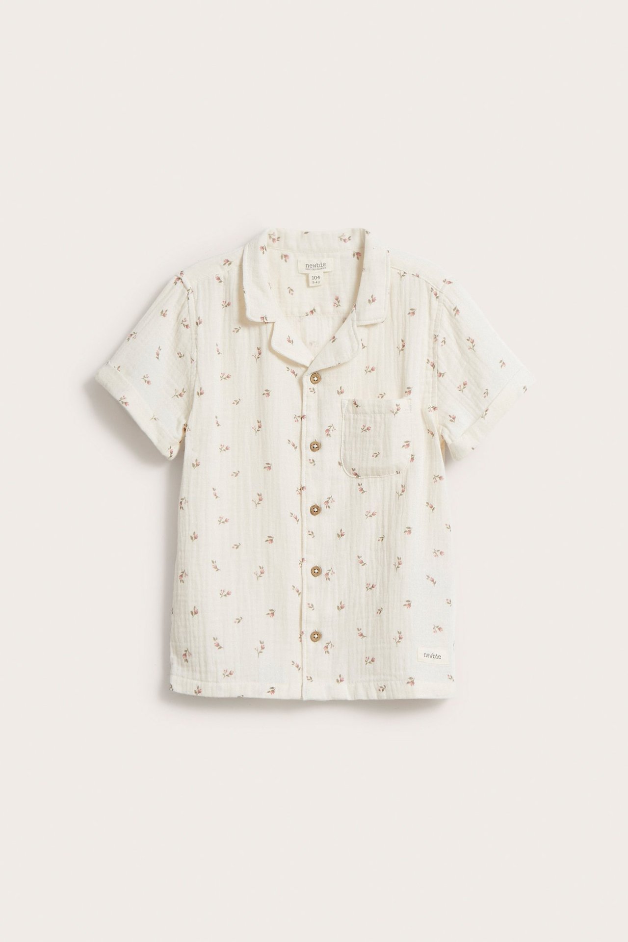 Front view of a kid's beige floral cotton muslin short-sleeve shirt with collar and front buttons.