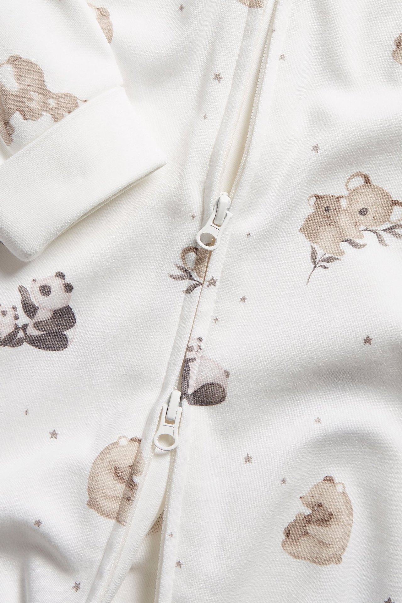 Close-up of an offwhite baby sleepsuit with brown animal pattern, fold-over cuffs, and front zipper.