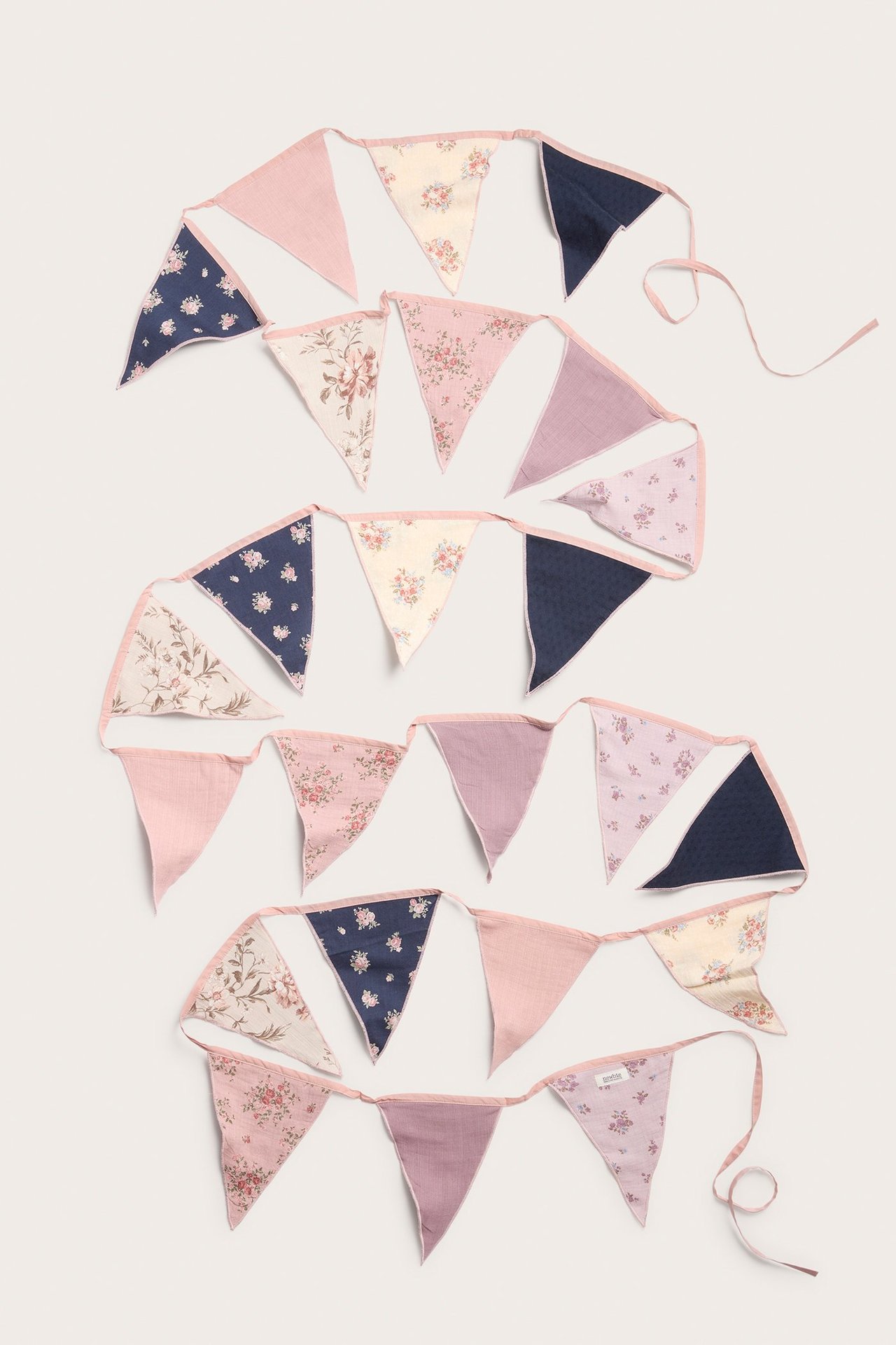 Bunting with floral and solid color pattern. Multi-colored with beige, pink and blue tones. Ties at the edge.