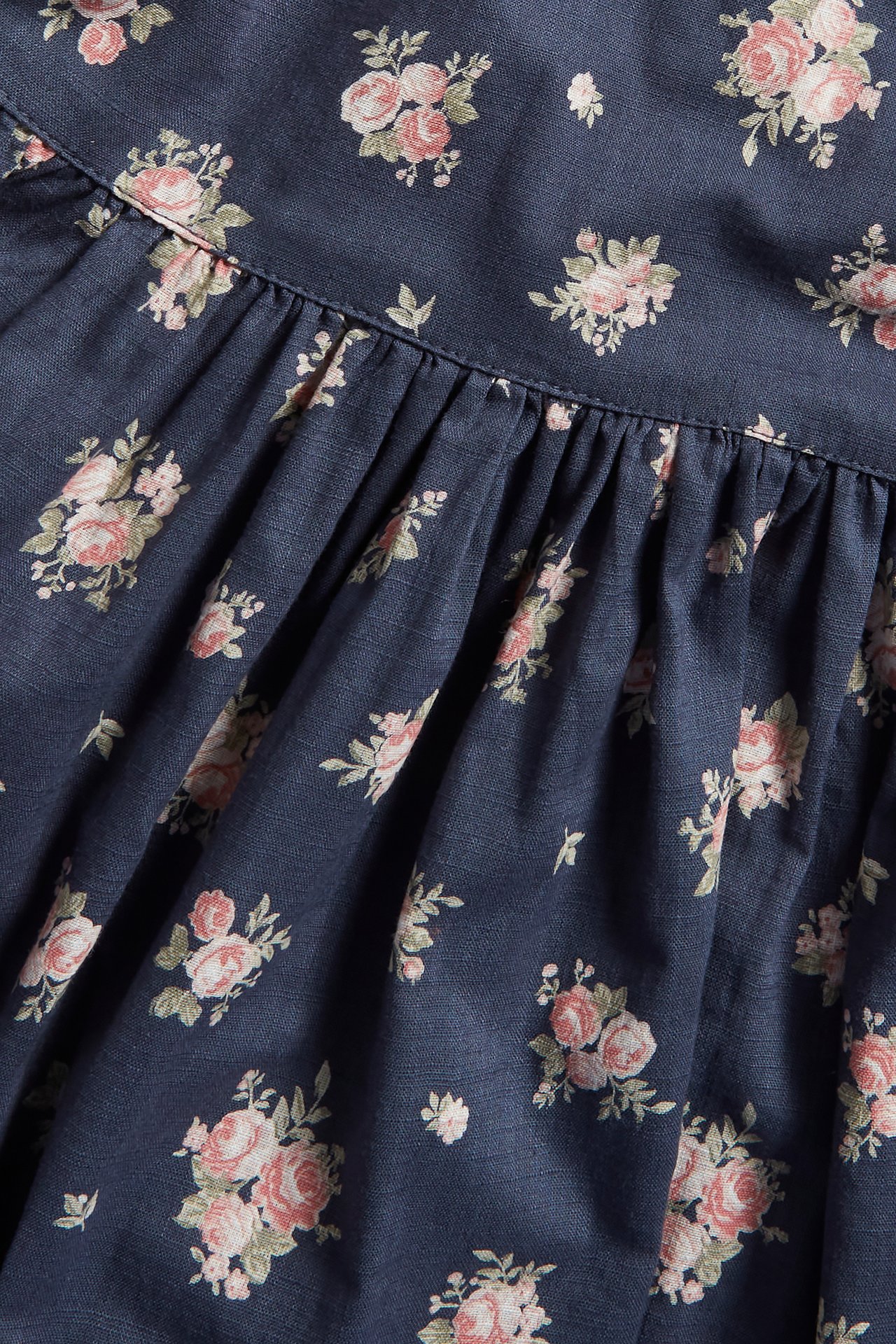 Nahaufnahme eines dunkelblauen Baumwollkleiderstoffs mit rosa Blumenmuster und geraffter Naht.