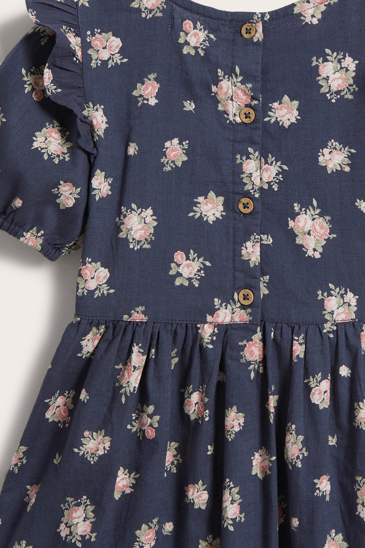 Rückenansicht eines dunkelblauen Baumwoll-Kinderkleides mit Blumenmuster, Puffärmeln und Knöpfen hinten.