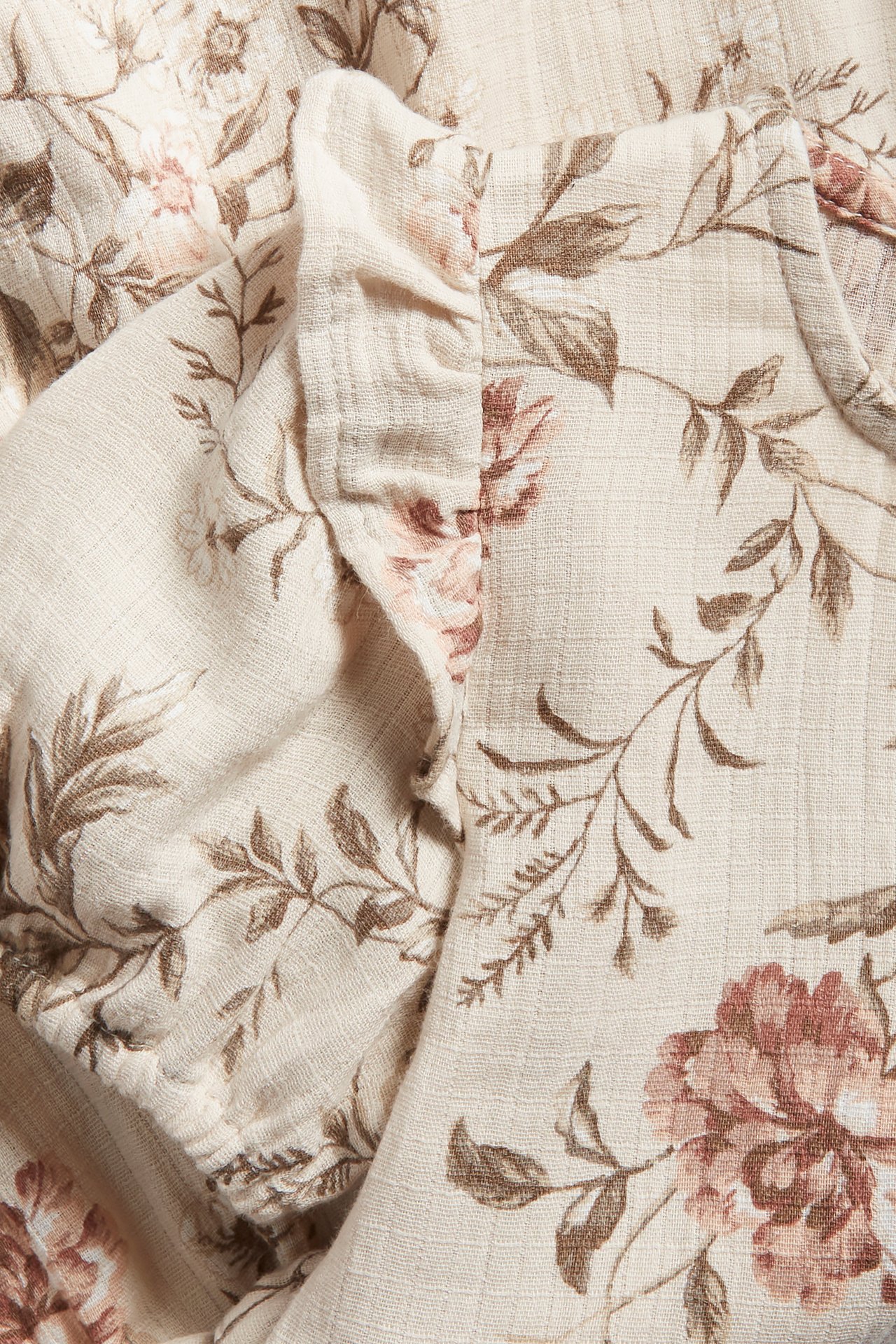 Close-up of a beige cotton floral dress with brown and pink flowers, featuring a puff sleeve and ruffle detail.