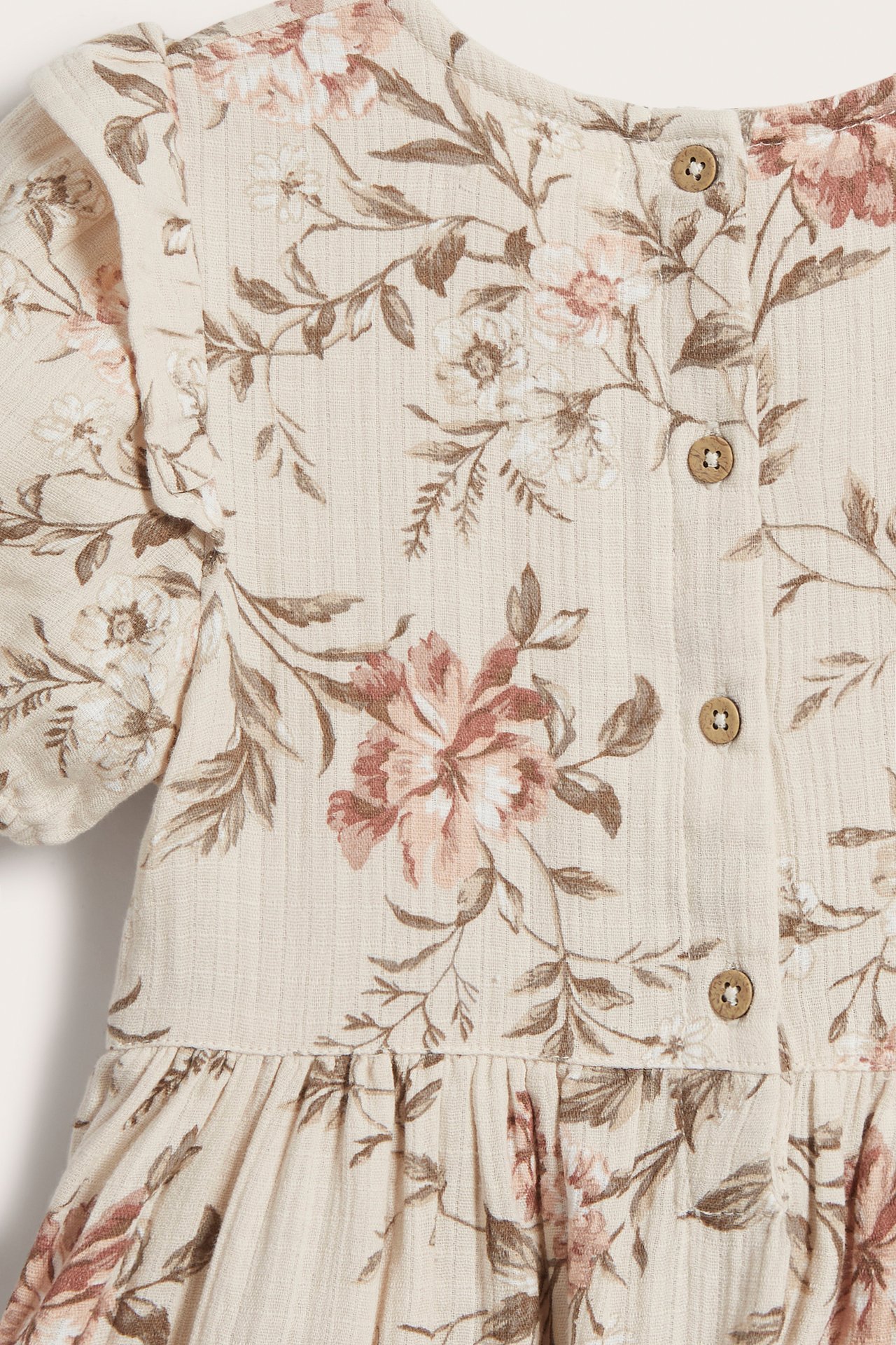 Close-up back view of a kid's beige ribbed floral cotton dress with puff sleeves and brown buttons.