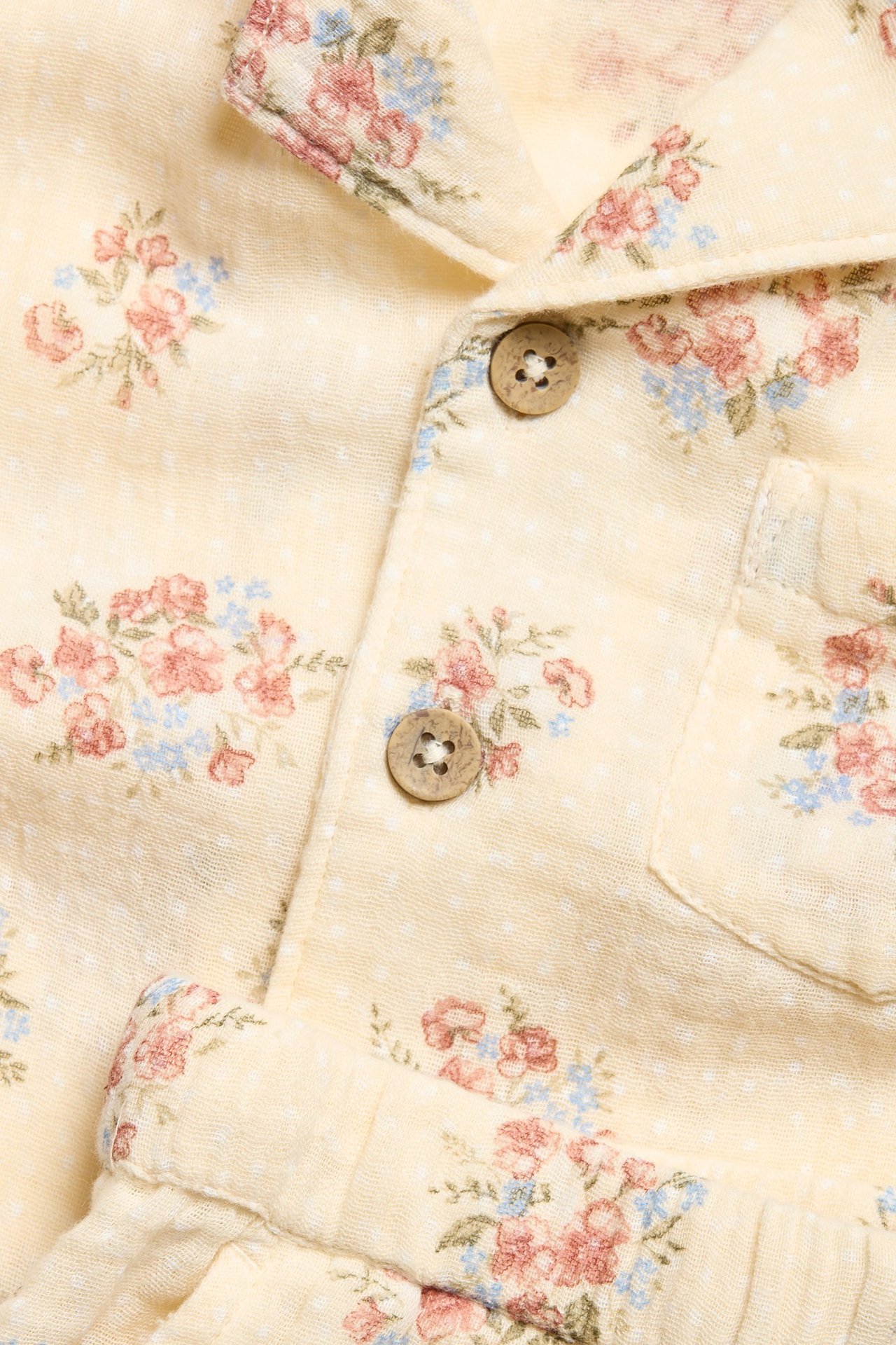 Close-up front view of a light yellow cotton floral pajama shirt with wooden buttons and matching shorts.