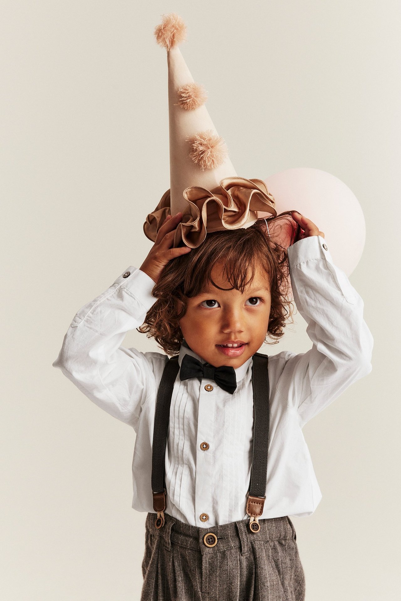 Vorderansicht, Kind trägt ein cremeweißes plissiertes Hemd mit schwarzer Fliege, dunkelgrauen Hosenträgern und Nadelstreifenhose.