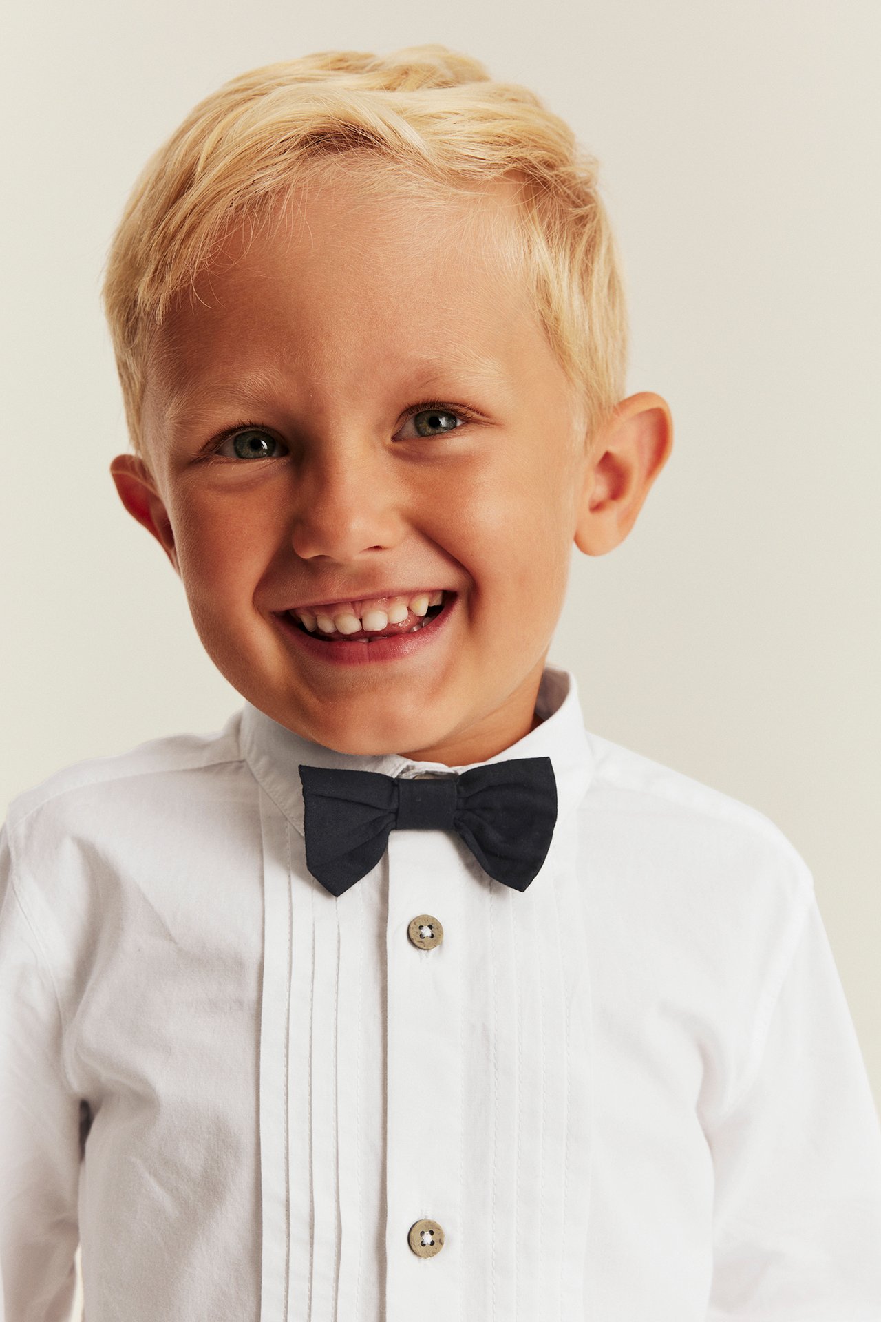Close-up of a kid wearing a white pleated shirt with wooden buttons and a black bow tie.