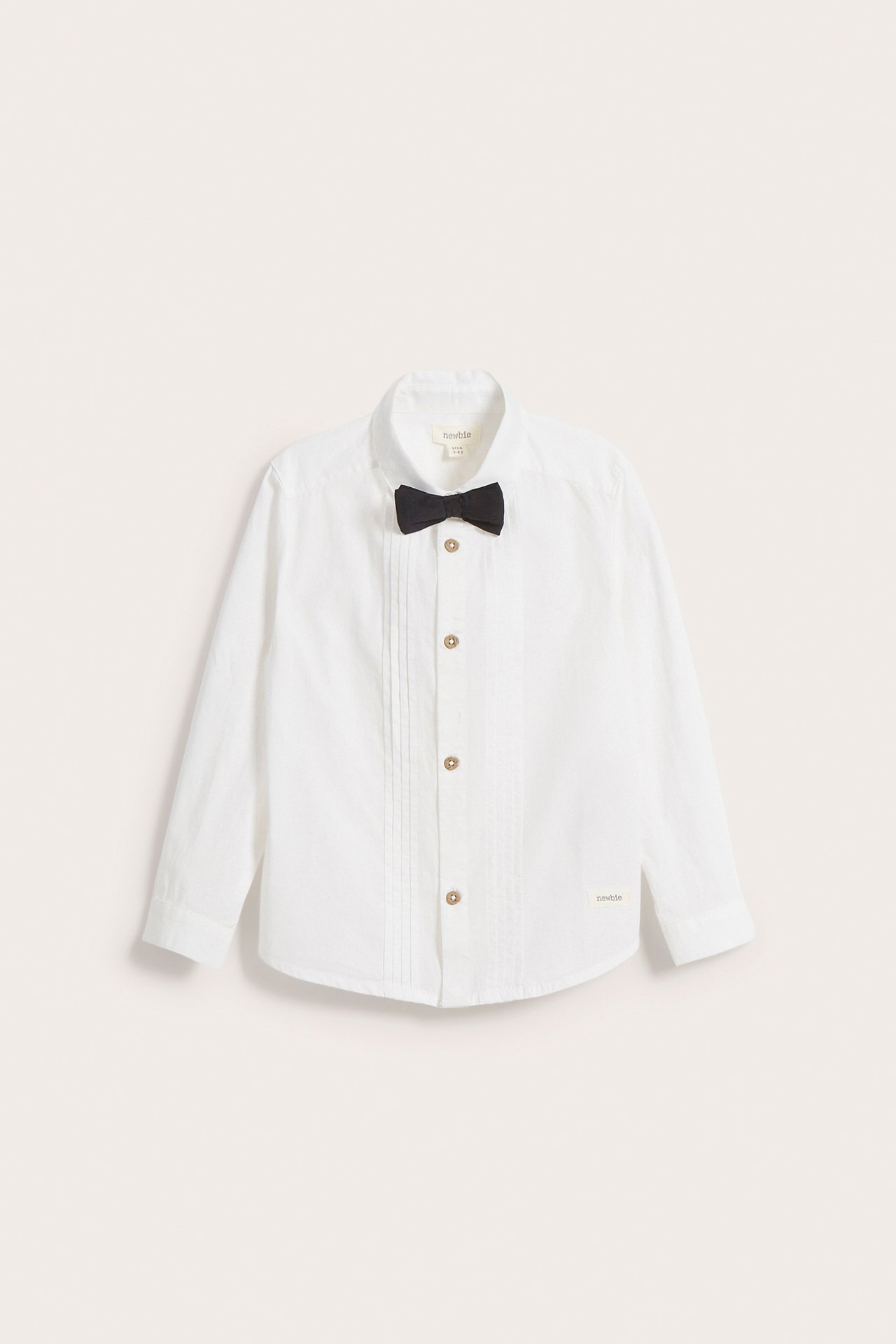 Front view: Kid's off-white cotton shirt with front pleats, button closure, and a black bow tie.