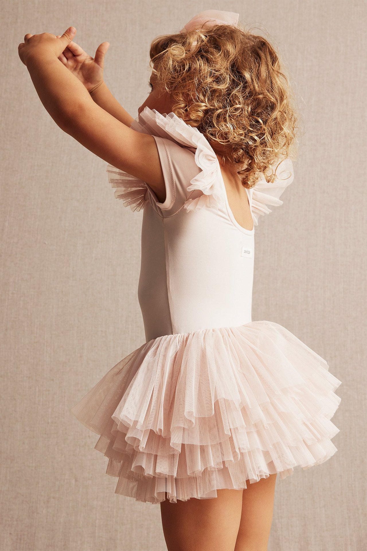 Side view of a kid wearing a light pink ballerina leotard with mesh ruffles and a hair bow.