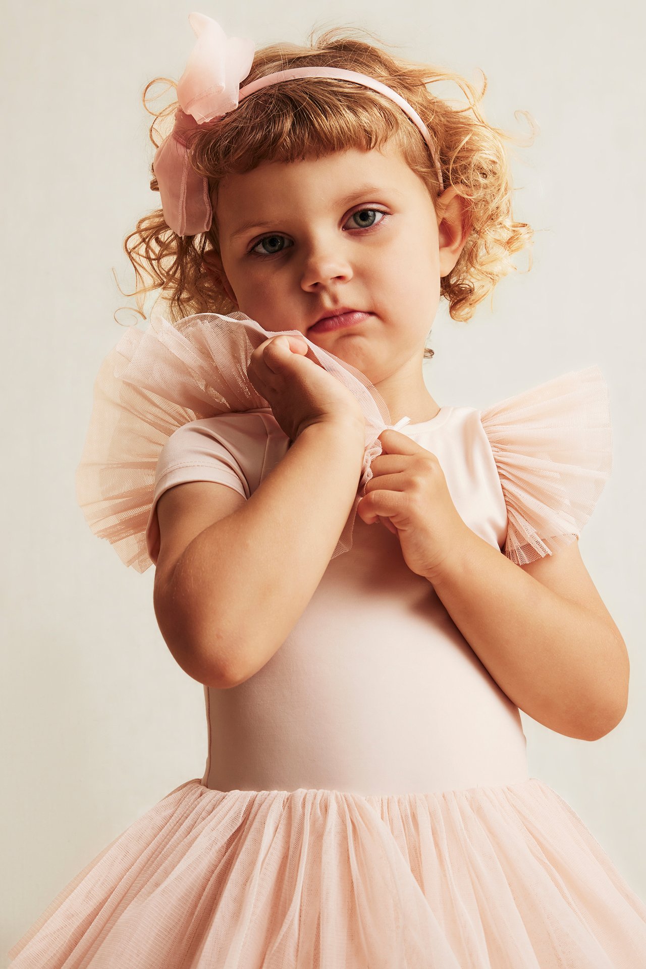 Front view: Kid in pink ballet leotard with tulle skirt, ruffle sleeves, and pink headband with bow.
