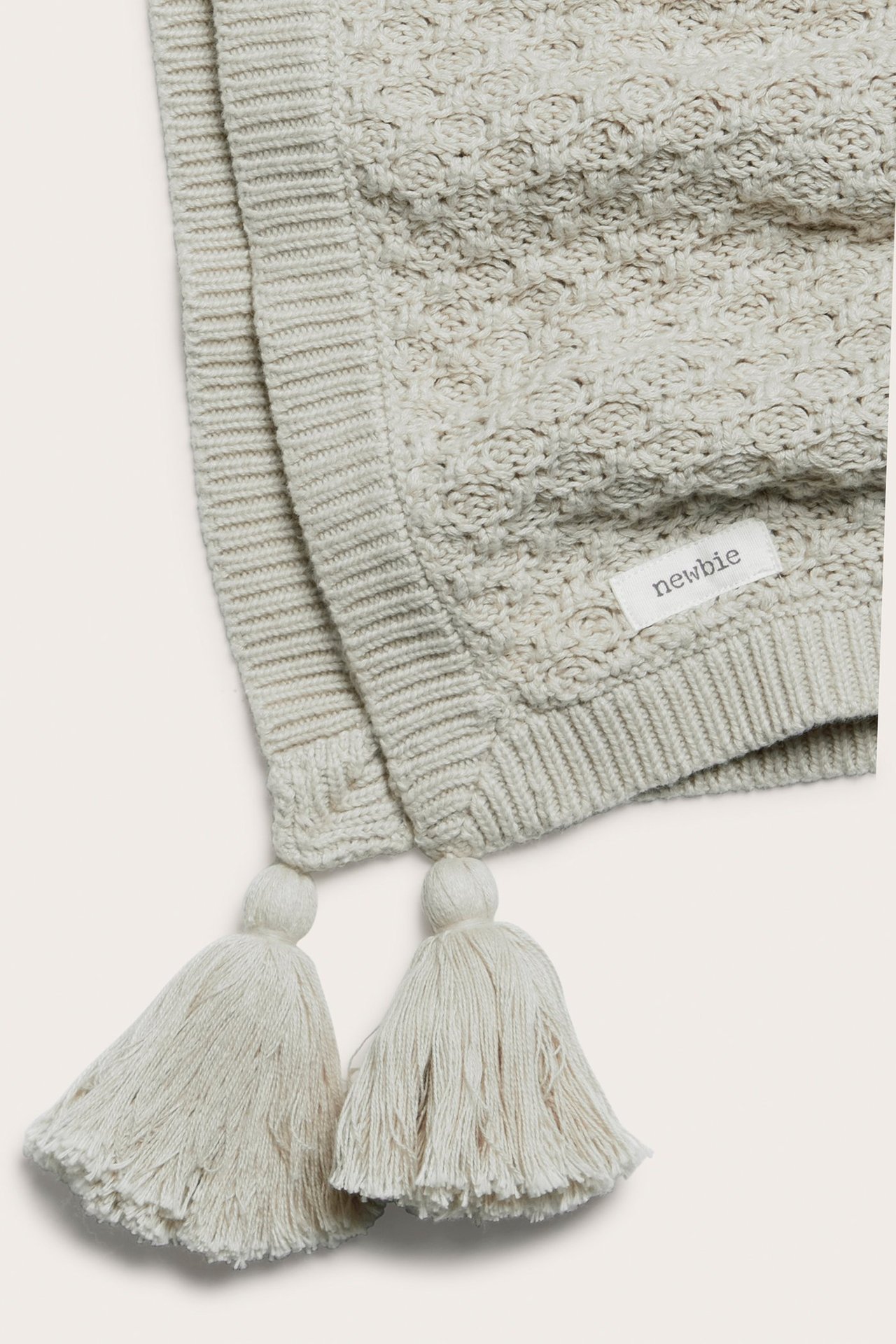 Nahaufnahme einer hellbeigen gemusterten Strick-Babydecke mit Quasten. Aus Bio-Baumwolle gefertigt.