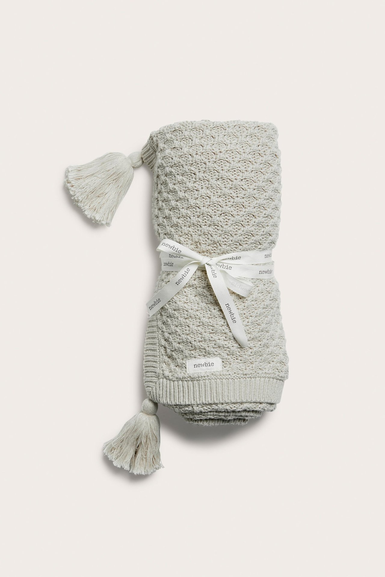 Vorderansicht einer gerollten hellgrünen gemusterten Strick-Babydecke mit Quasten, mit weißem Band gebunden.