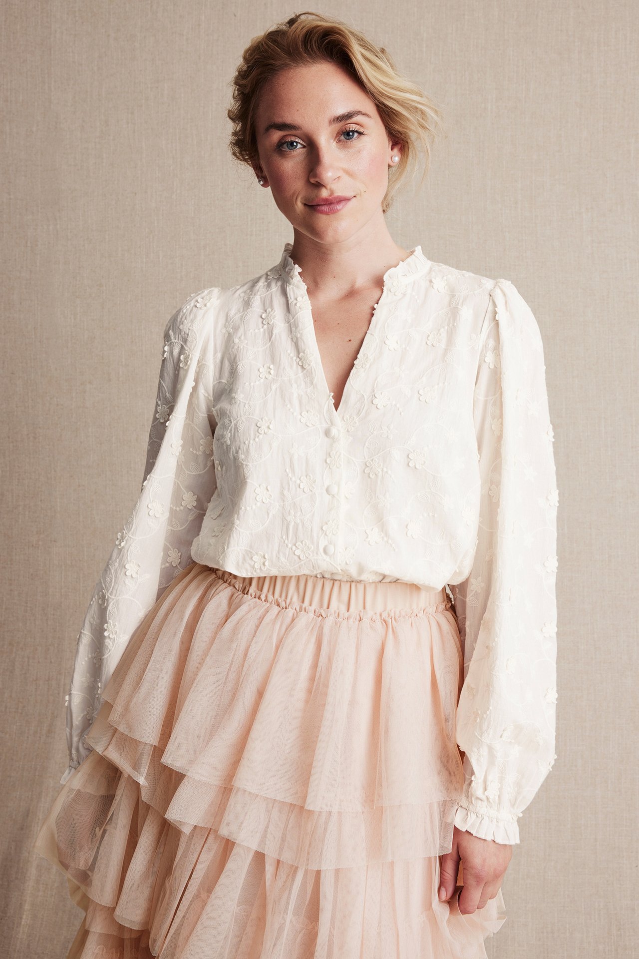 Front view: Woman in offwhite embroidered cotton blouse with frills and light pink tiered tulle skirt.