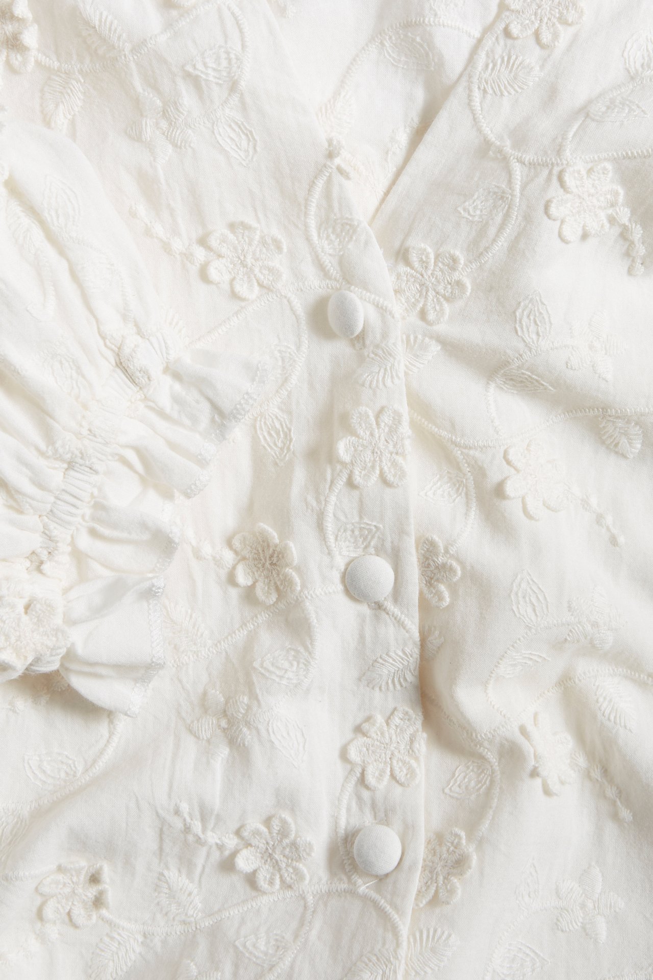 Close-up of an off-white organic cotton blouse with allover floral embroidery and covered front buttons.