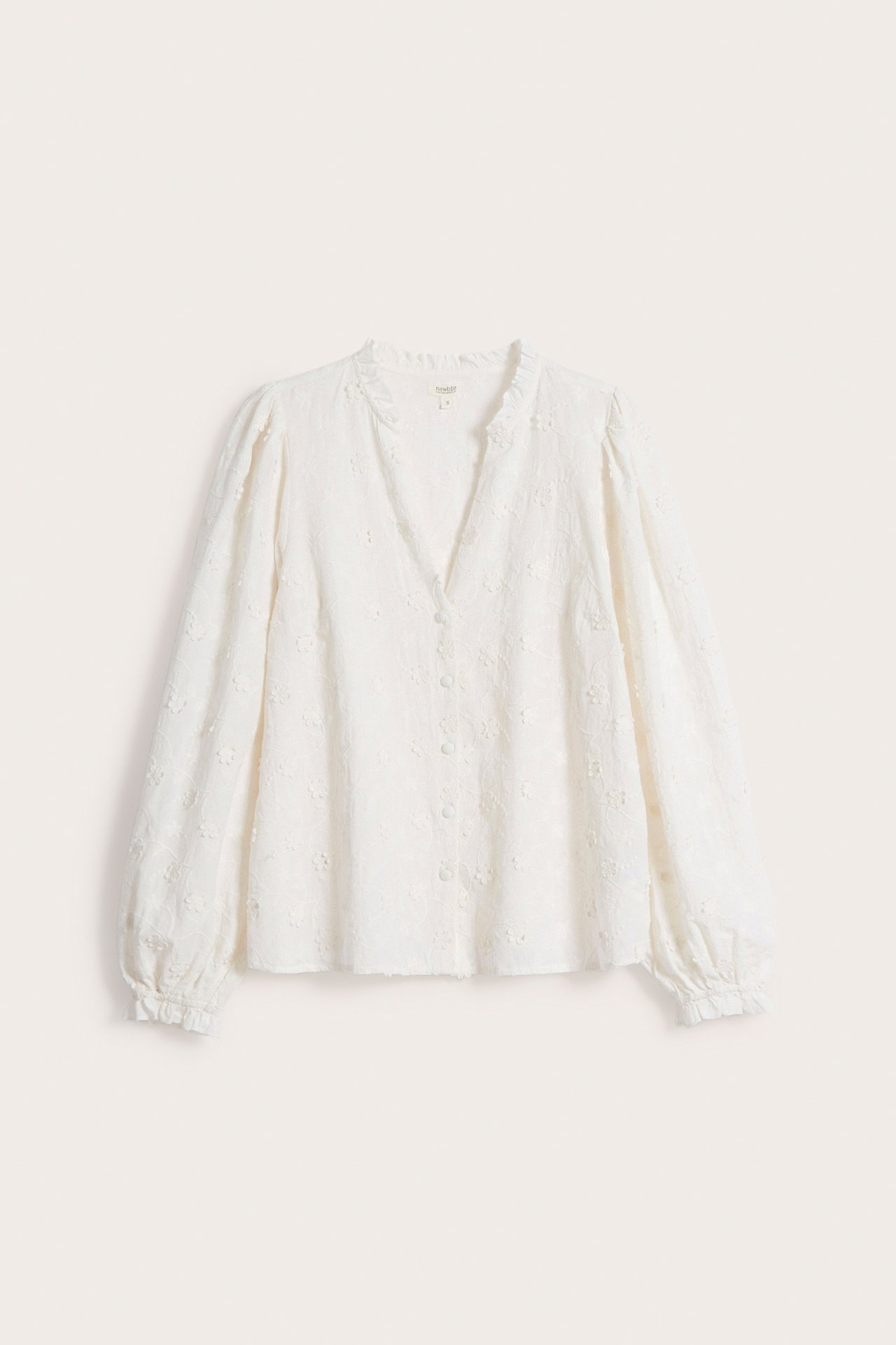 Front view of an off-white woman's blouse with allover floral embroidery, frilled neckline, and covered buttons.