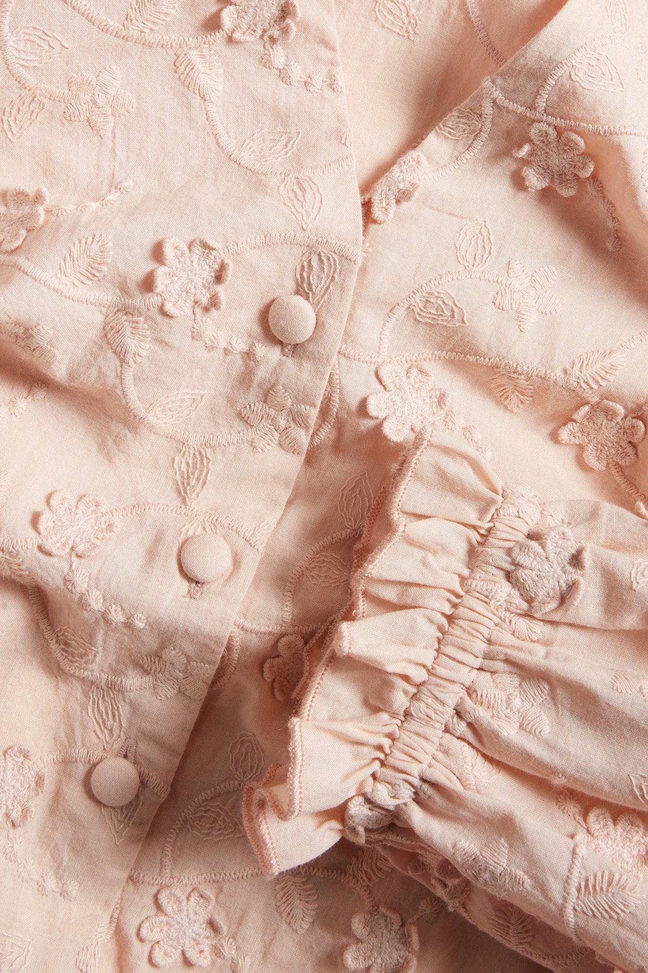 Nahaufnahme einer rosa Baumwollbluse mit Blumenstickerei, 3D-Blumen, bezogenen Knöpfen und Rüschenmanschette.